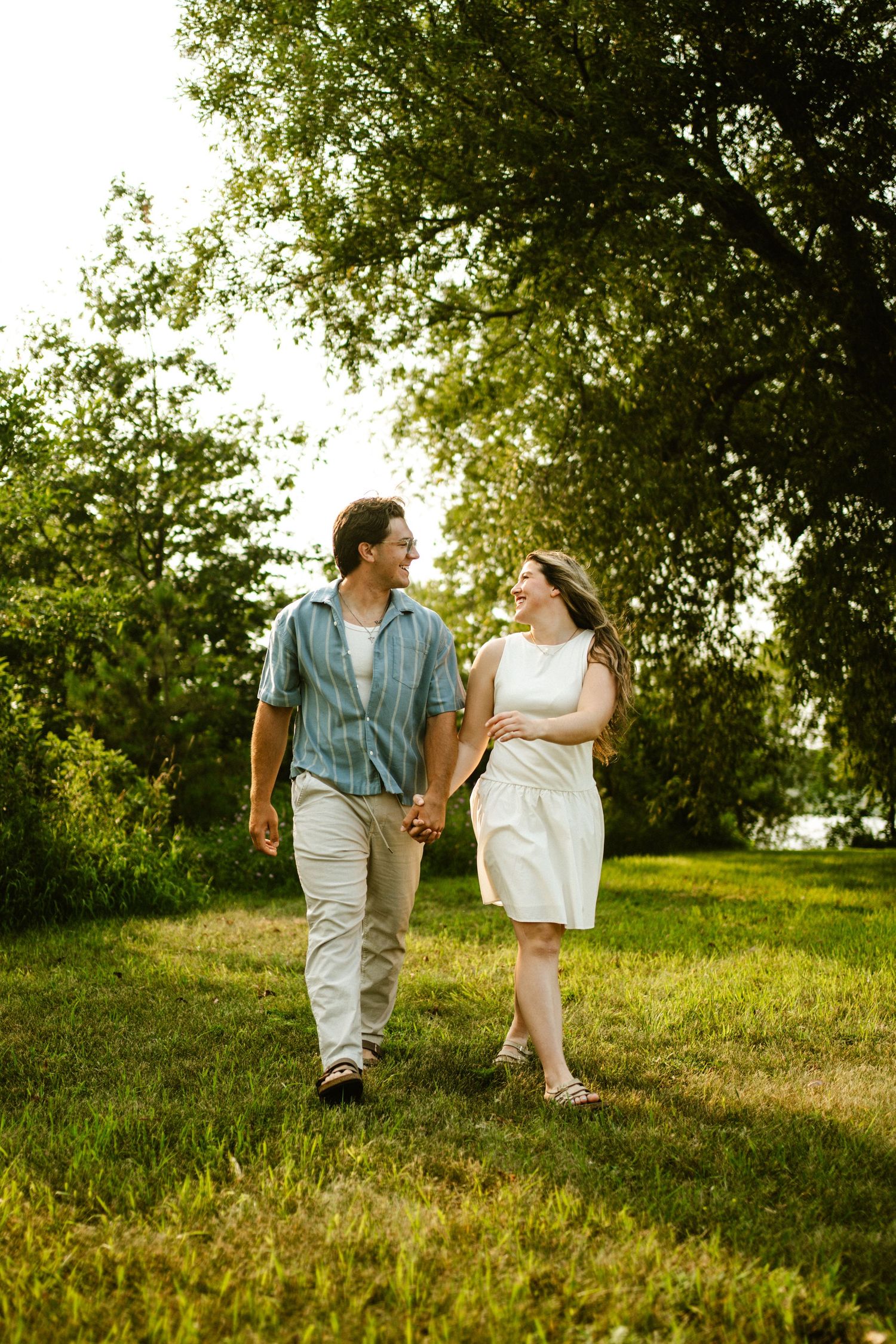 Happy couple holds hands walking through lush green park on a sunny summer day.