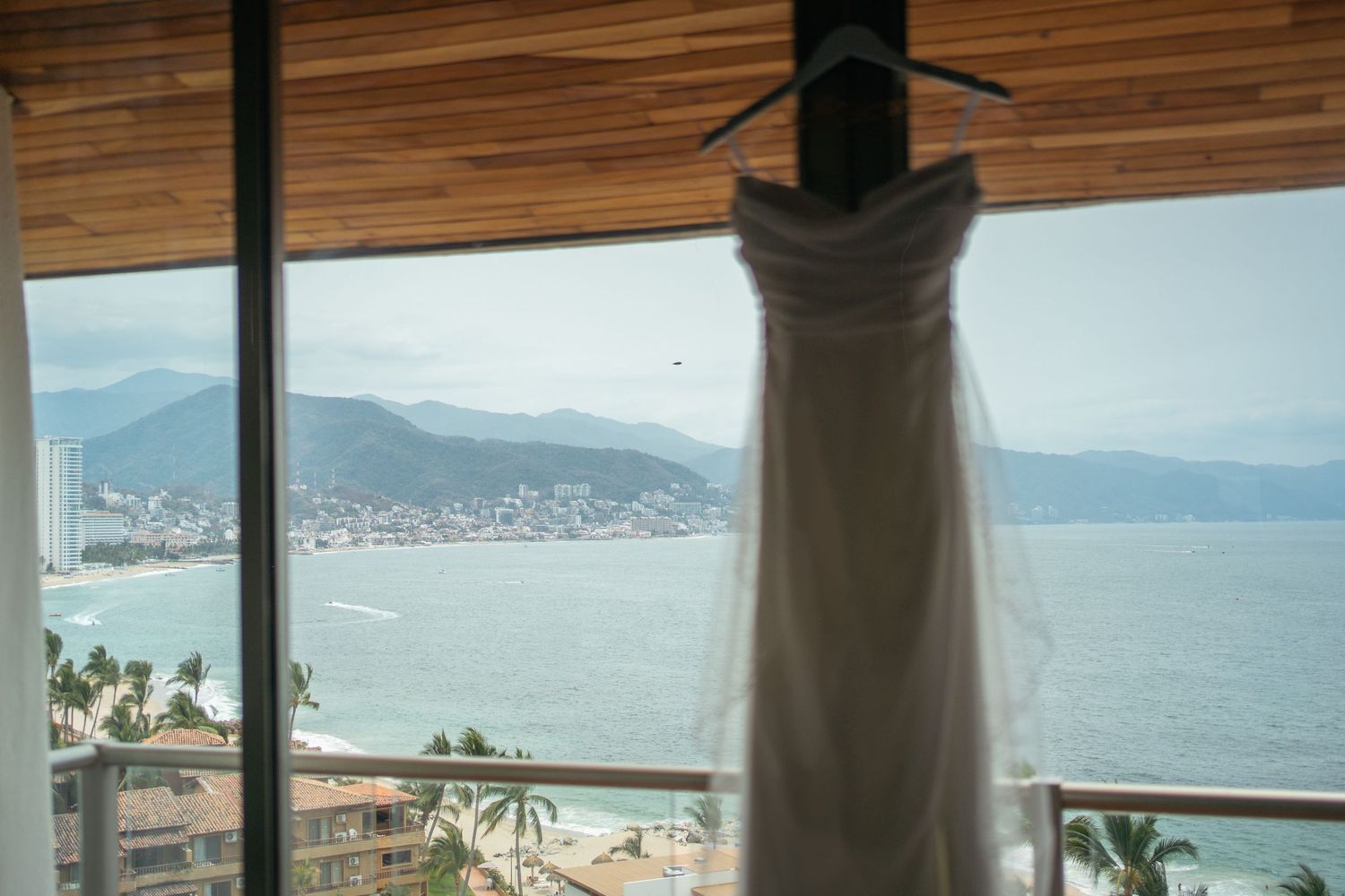 Elegant white wedding dress hanging by a window with a stunning coastal mountain view in the background.