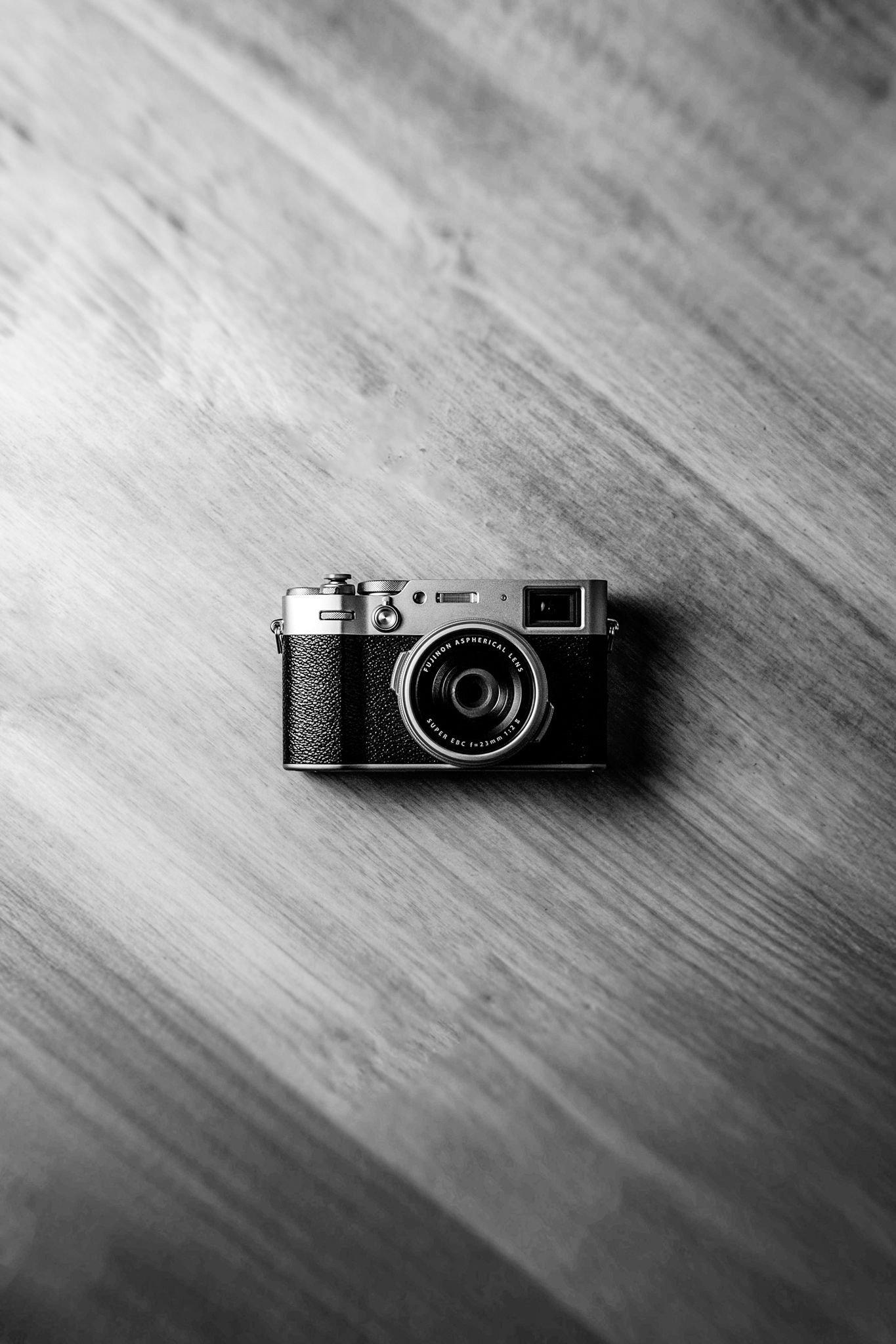 A black and white overhead shot of a vintage compact camera resting on a wooden surface.