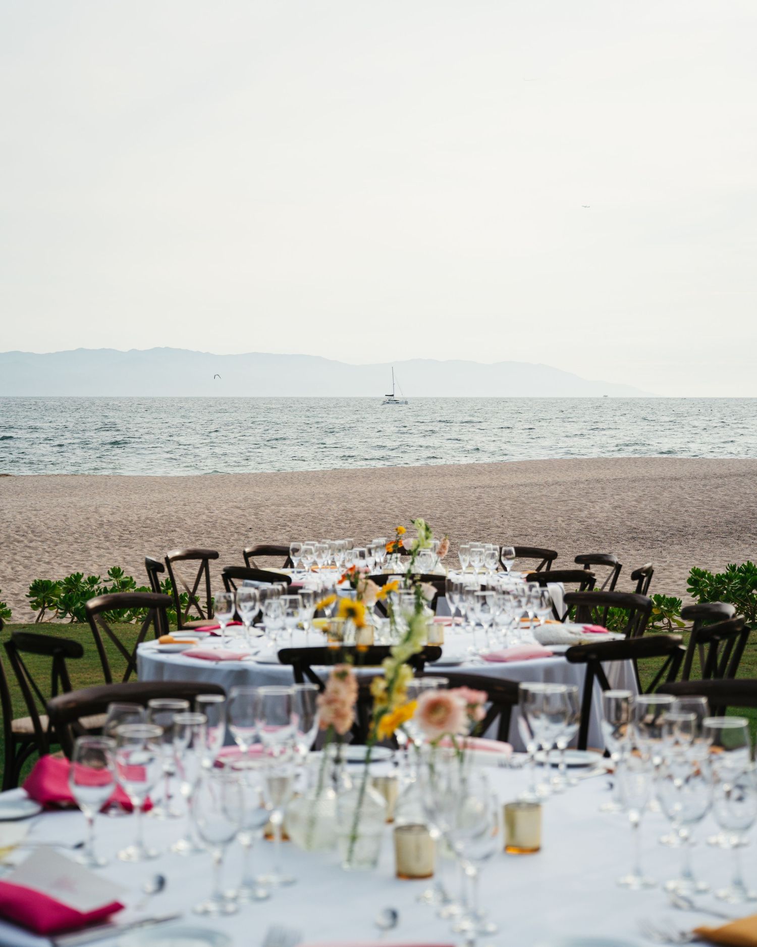 Elegant beachside wedding reception tables set with glassware and floral centerpieces overlooking the ocean.