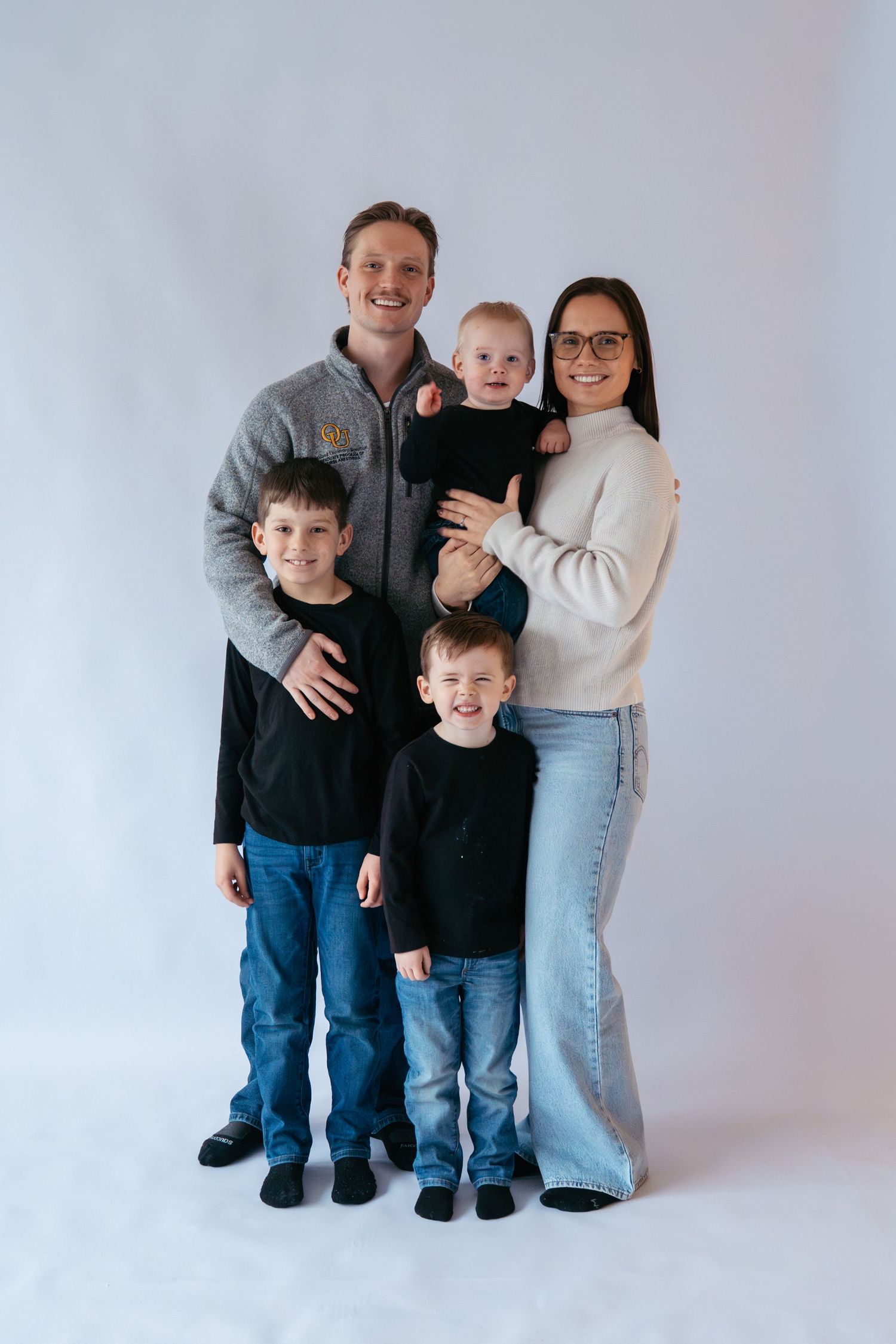 Happy family of five posing together in casual attire against a clean white studio background.