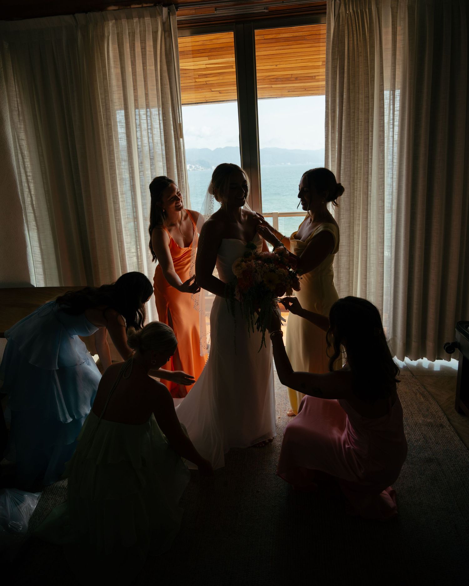 Silhouette of bride and bridesmaids preparing near a bright window before the wedding ceremony.