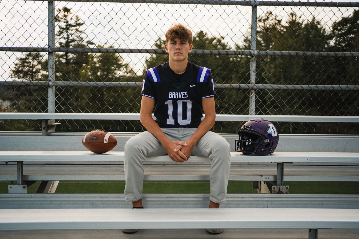 Teen football player in Braves jersey number 10 sitting on bleachers with helmet and ball.