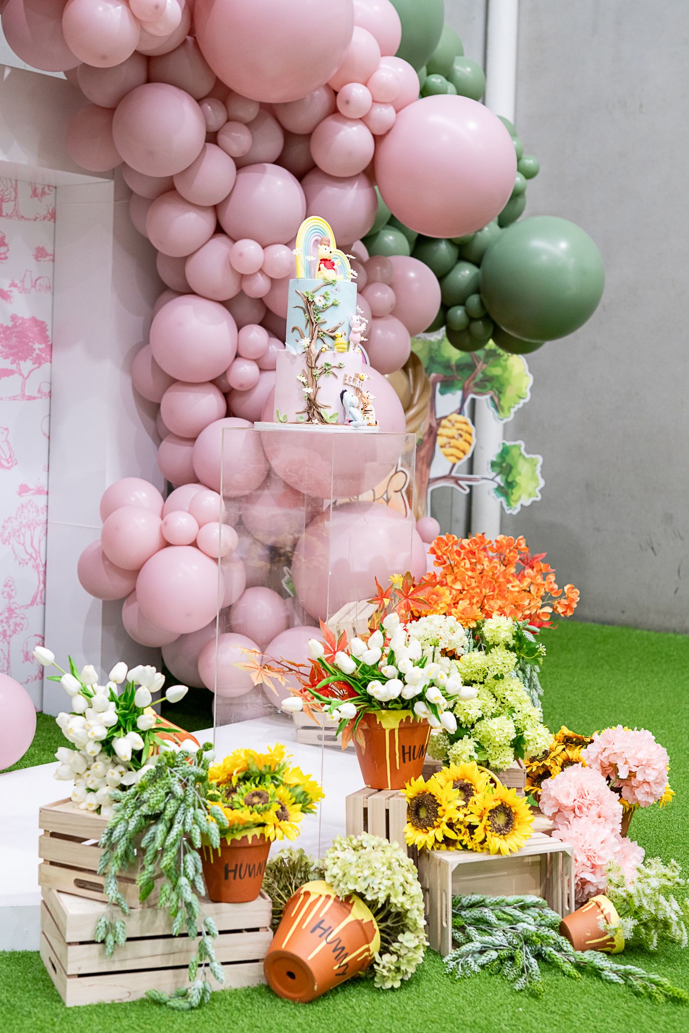 Pink balloon arch with floral displays arranged on wooden crates against a decorated backdrop.