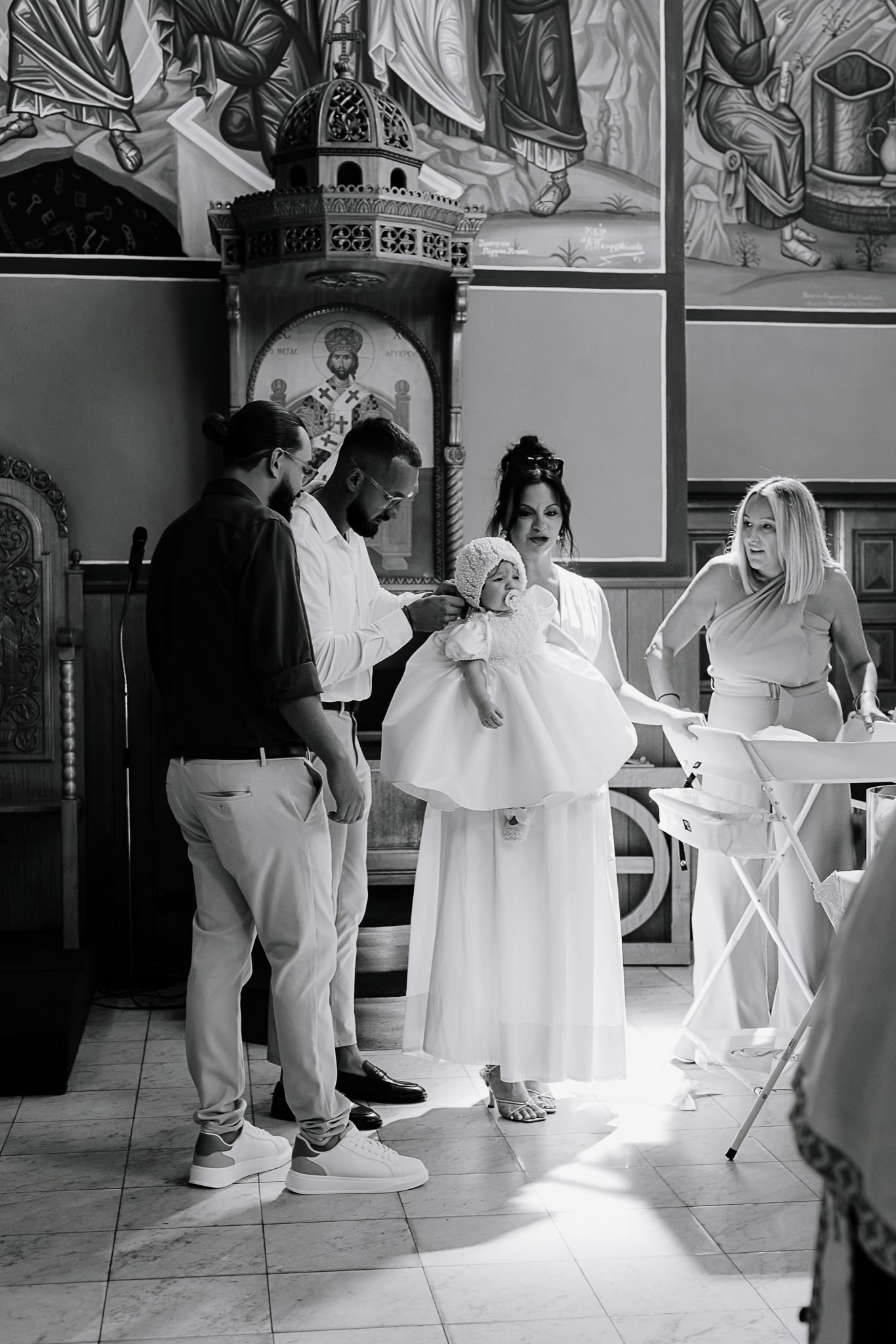 Group gathered in church for baptism ceremony with baby in white dress.