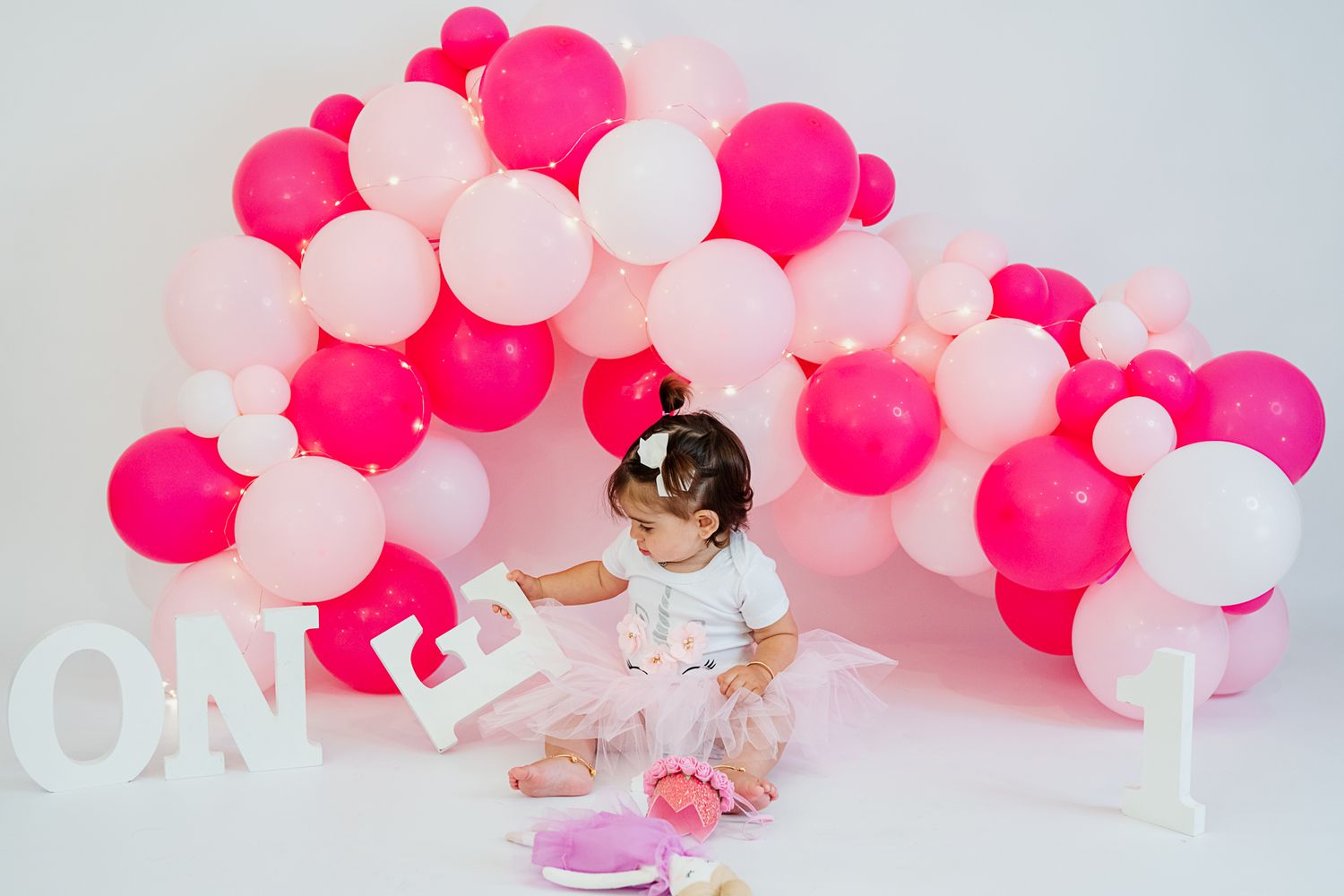 Birthday setup with pink balloon arch and white 'ONE' letters for first birthday celebration.