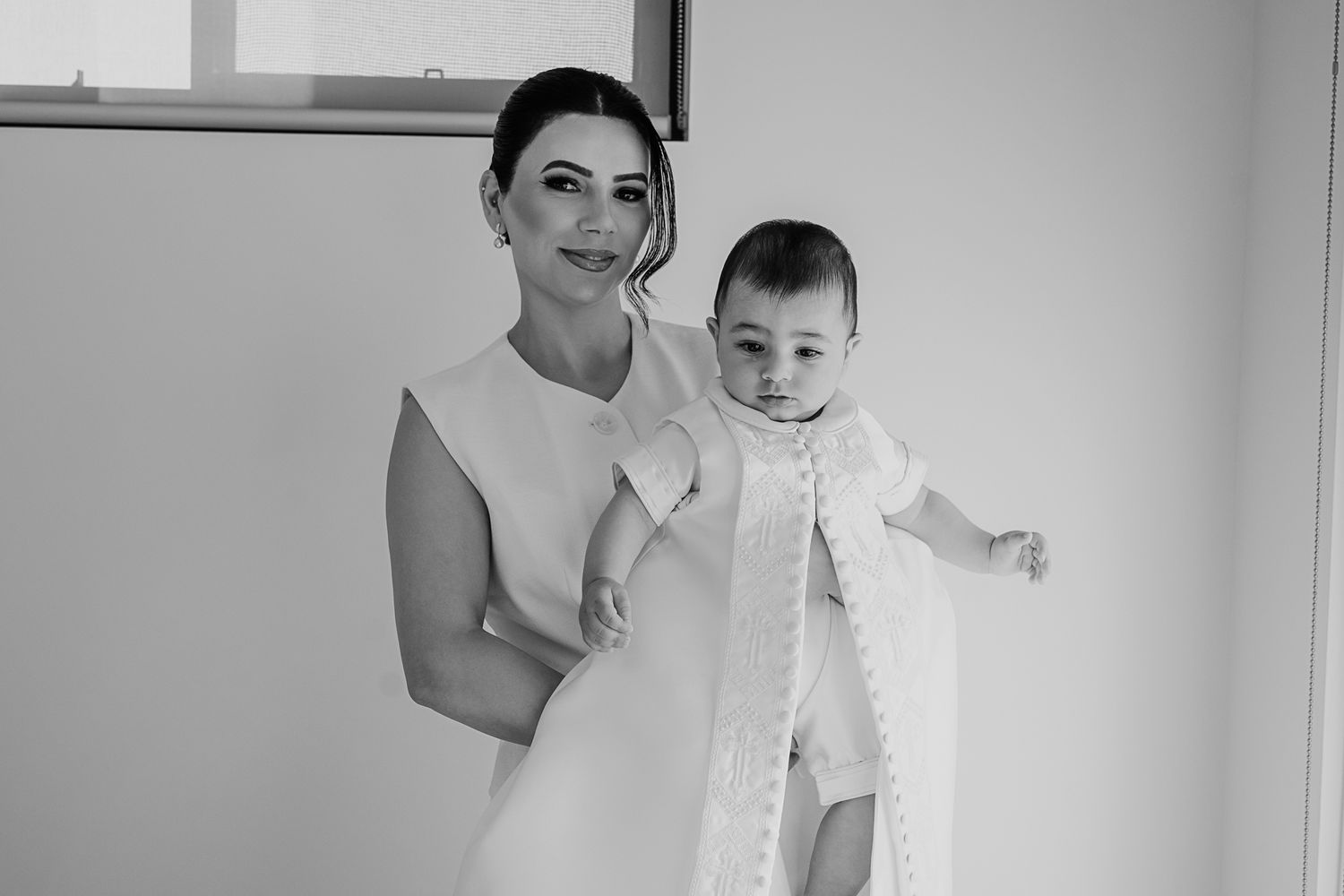 Black and white photo of a woman in white dress holding a smiling baby.