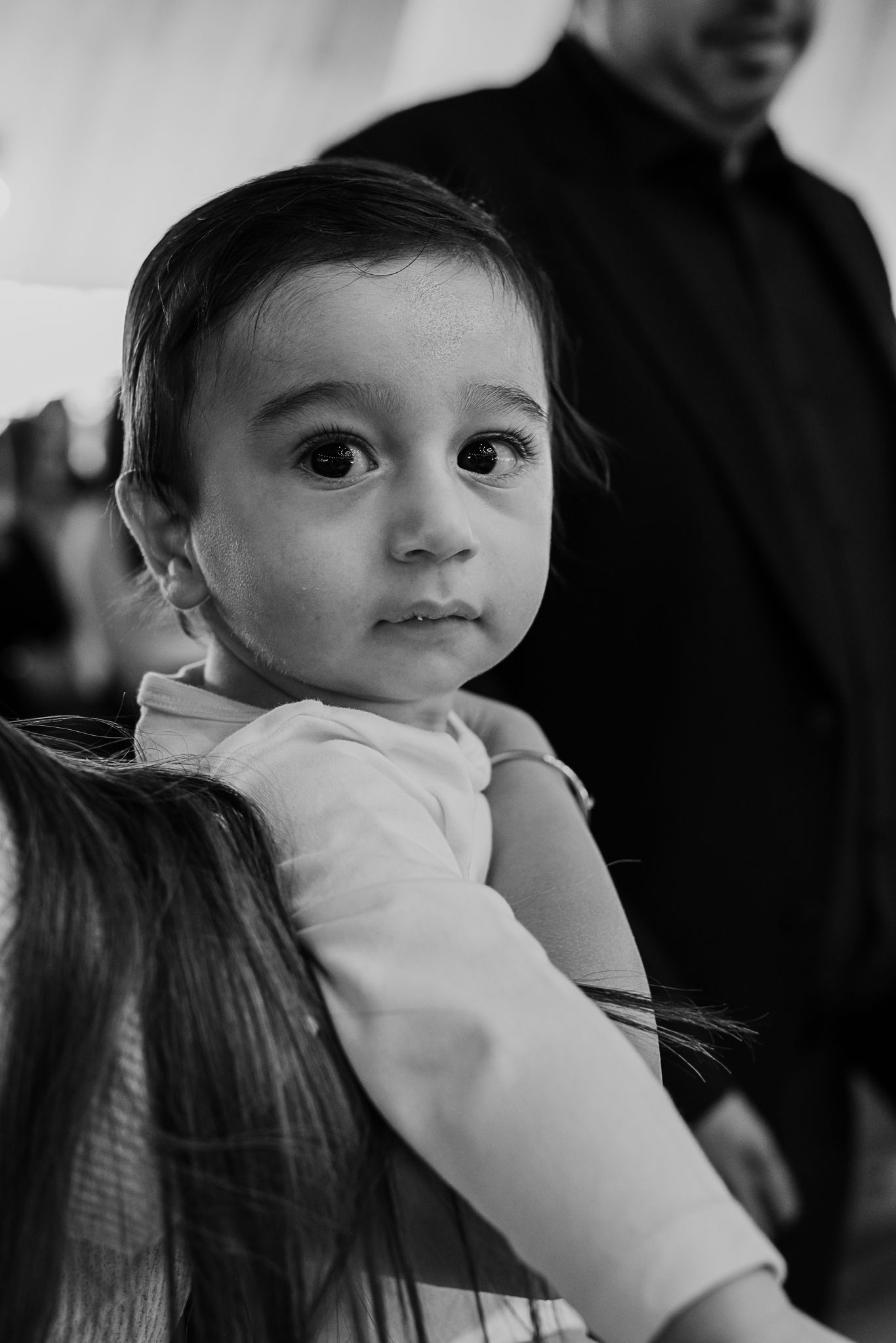 Black and white portrait of a young toddler in a light colored shirt looking to the side with large expressive eyes.
