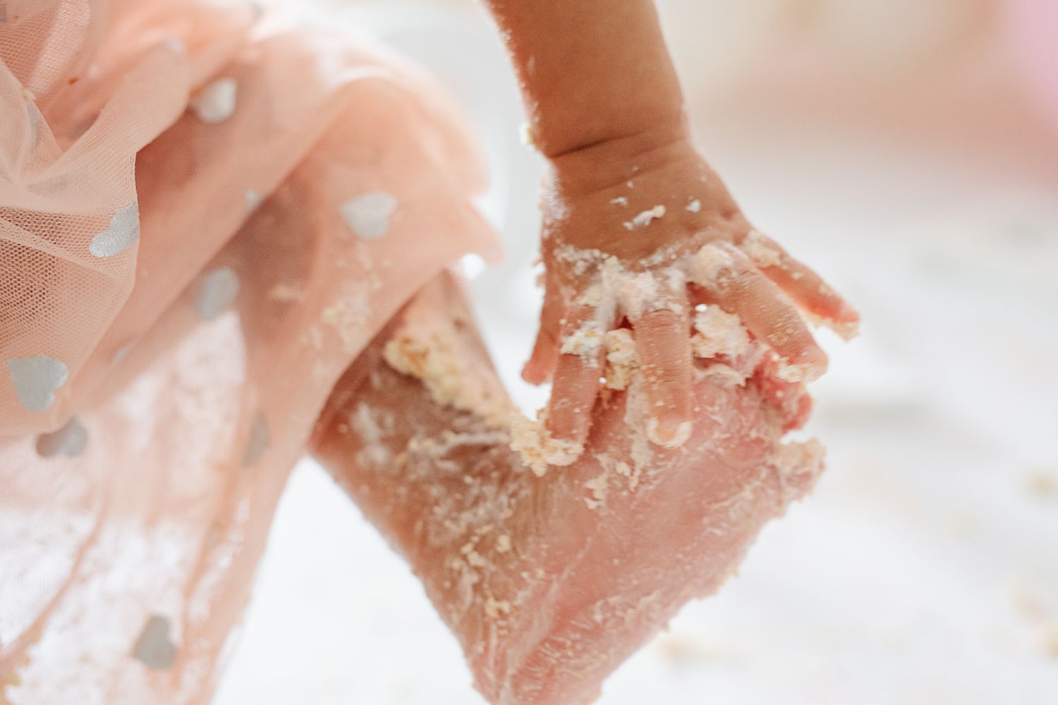 Close-up of small hands covered in white cake frosting during celebration.