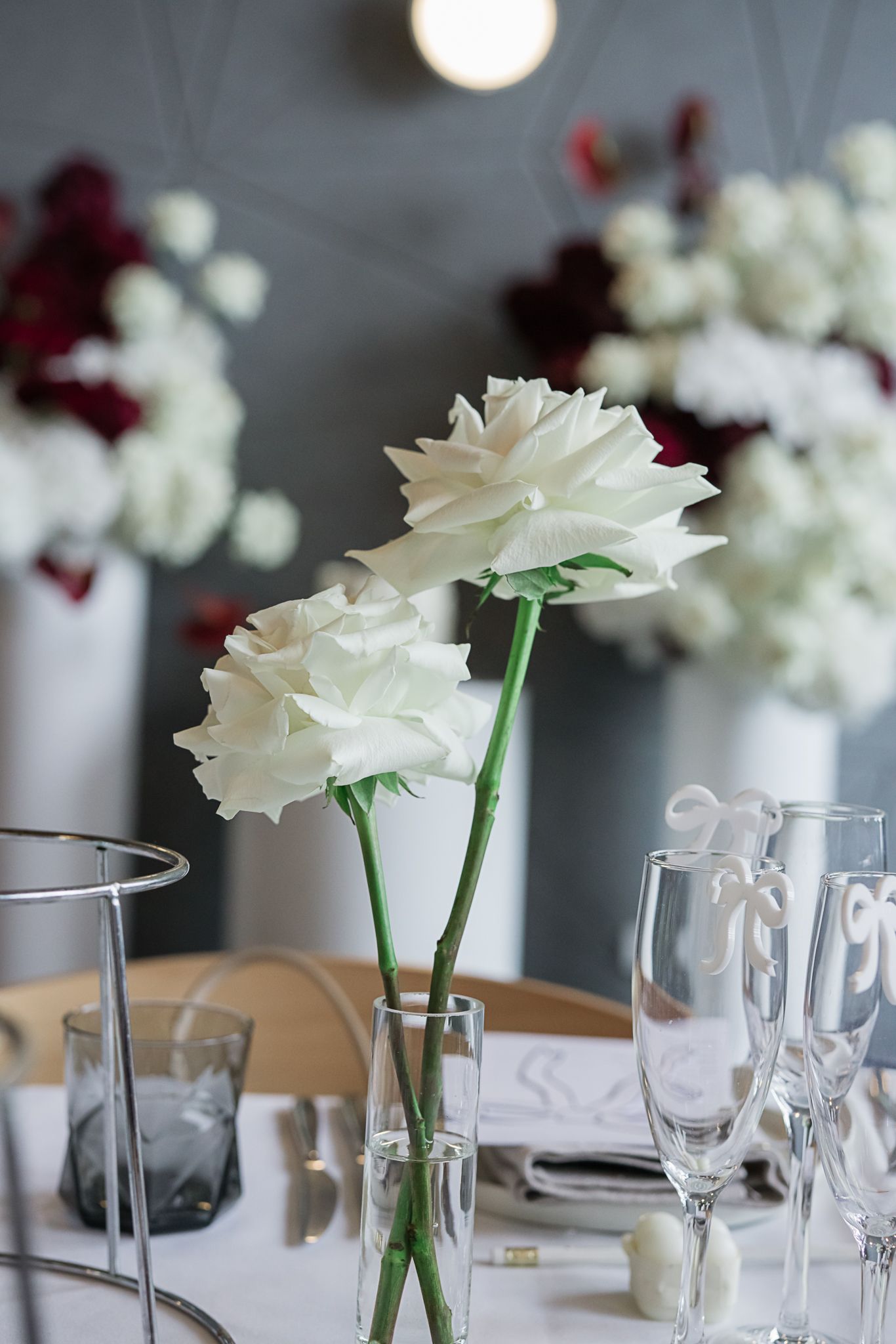 White roses in a glass vase with champagne flutes set on an elegant table setting.