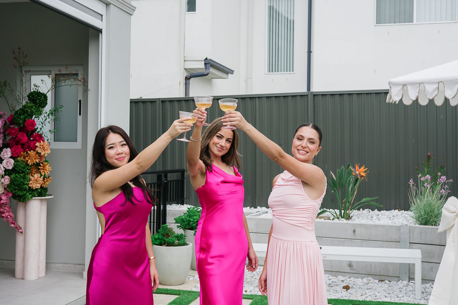 Wedding celebration with bridesmaids in pink dresses toasting with champagne glasses in outdoor setting.