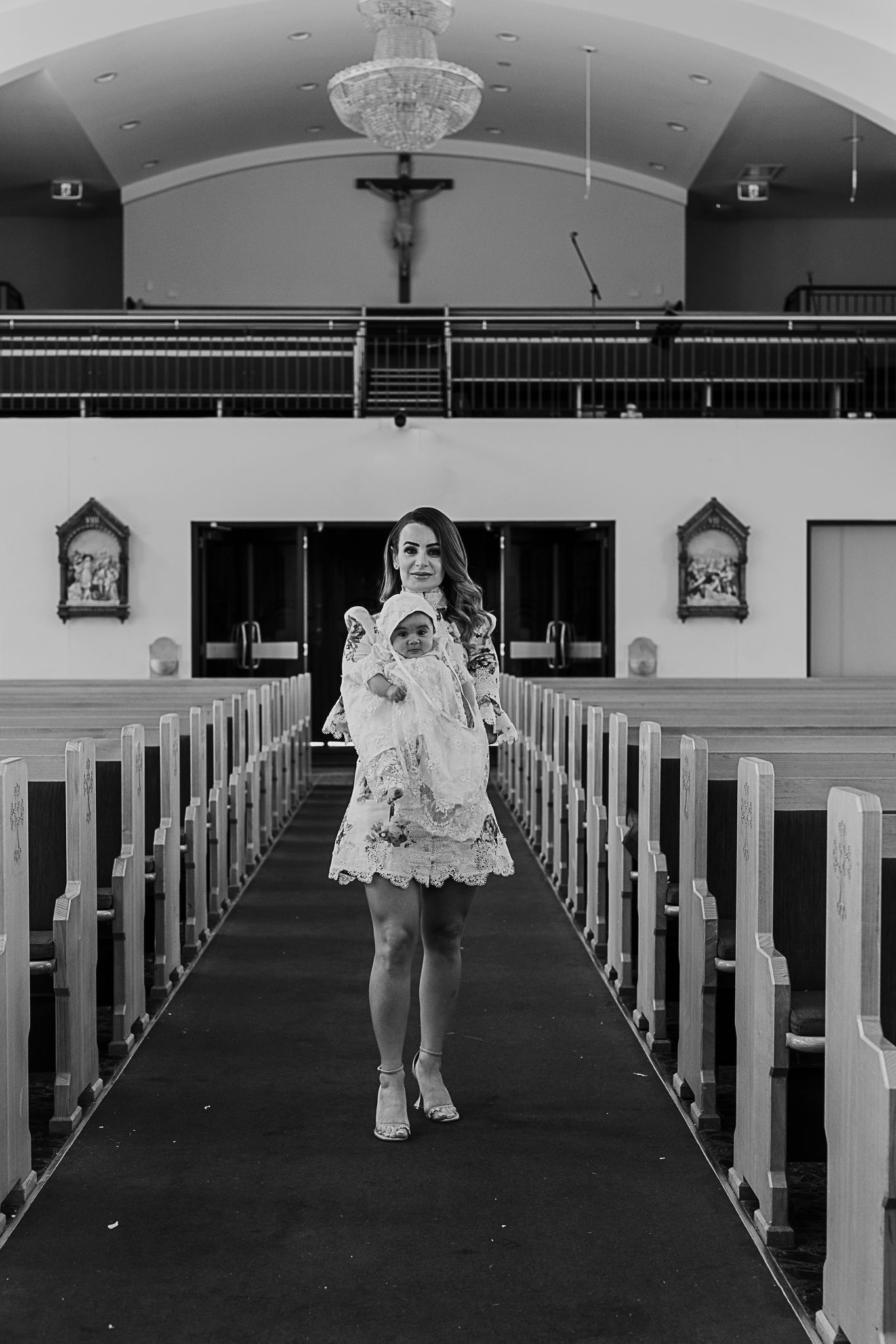 A black and white photograph showing elegant feminine silhouette standing in a church aisle between wooden pews.