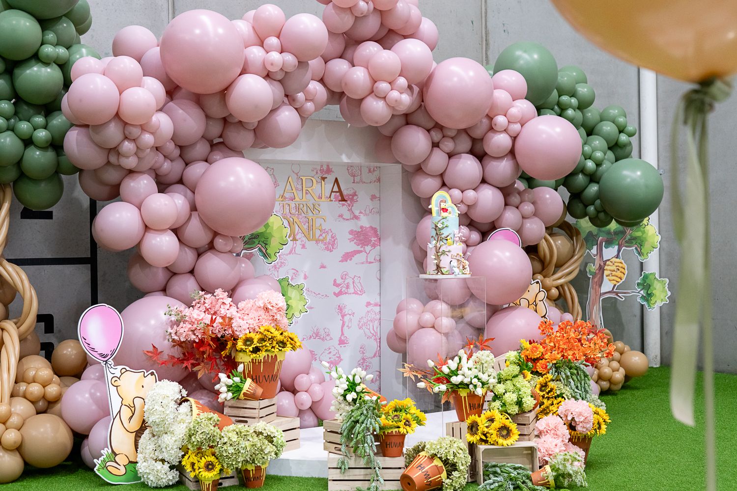 Pink and green balloon arch with floral decorations for party setup.