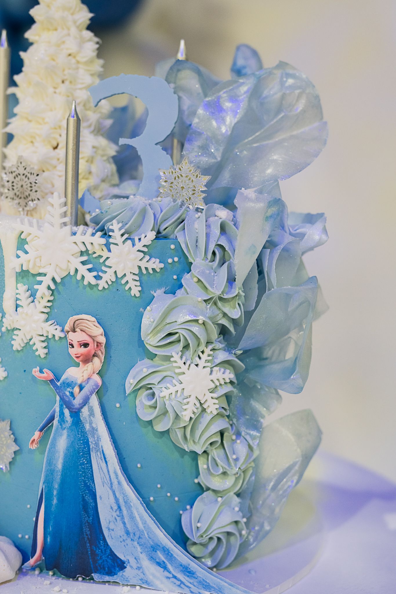 Close-up of winter-themed cake with blue frosting, delicate snowflakes, and ruffled sugar decorations.