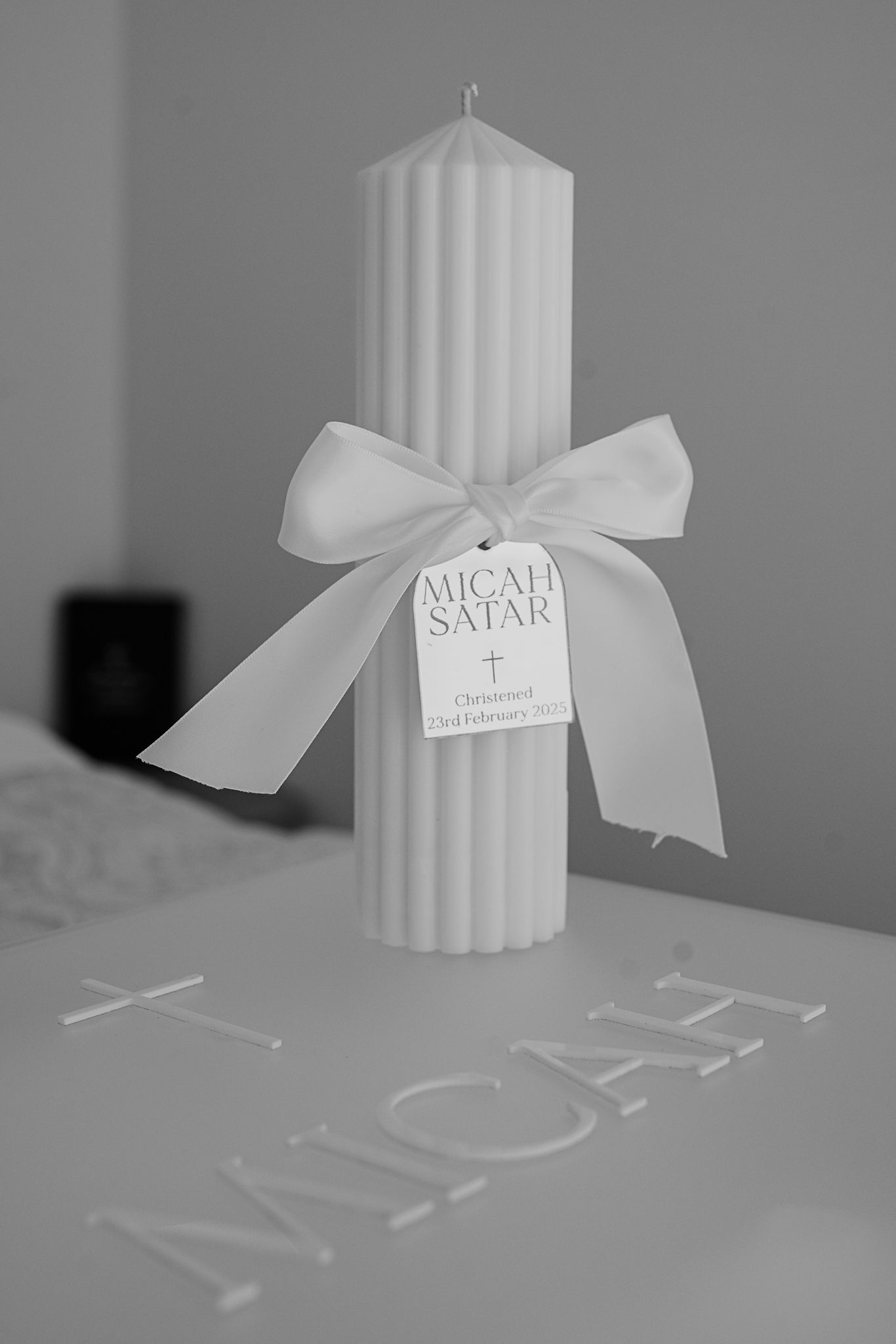 White decorative baptism candle with ribbon and name tag against grey background.