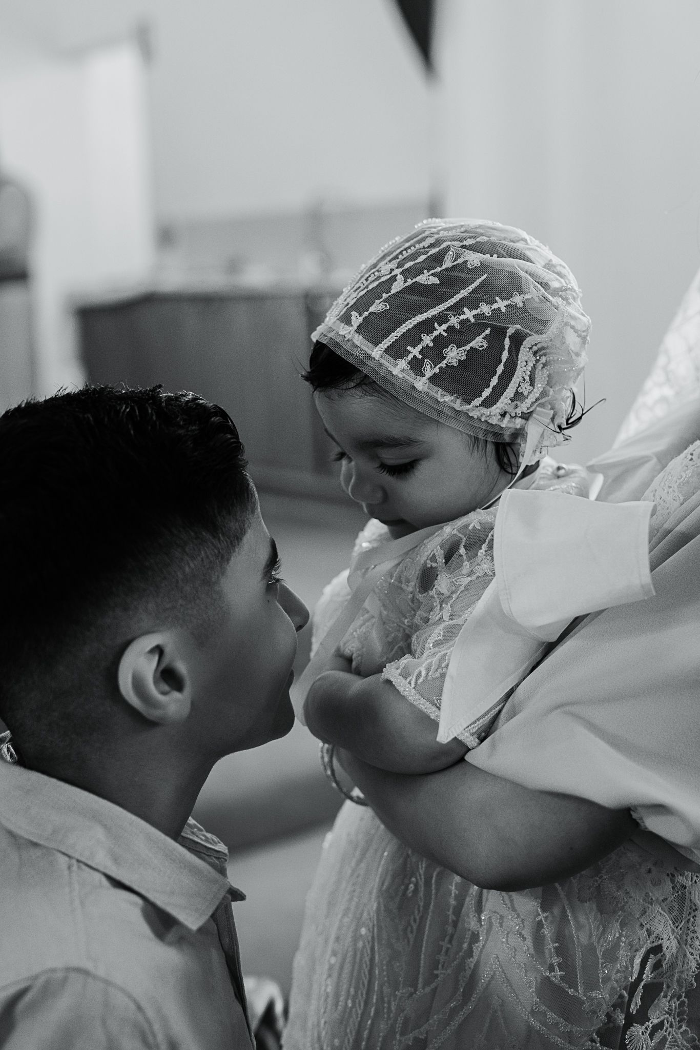 Intimate moment shared between parent and baby dressed in white christening gown.