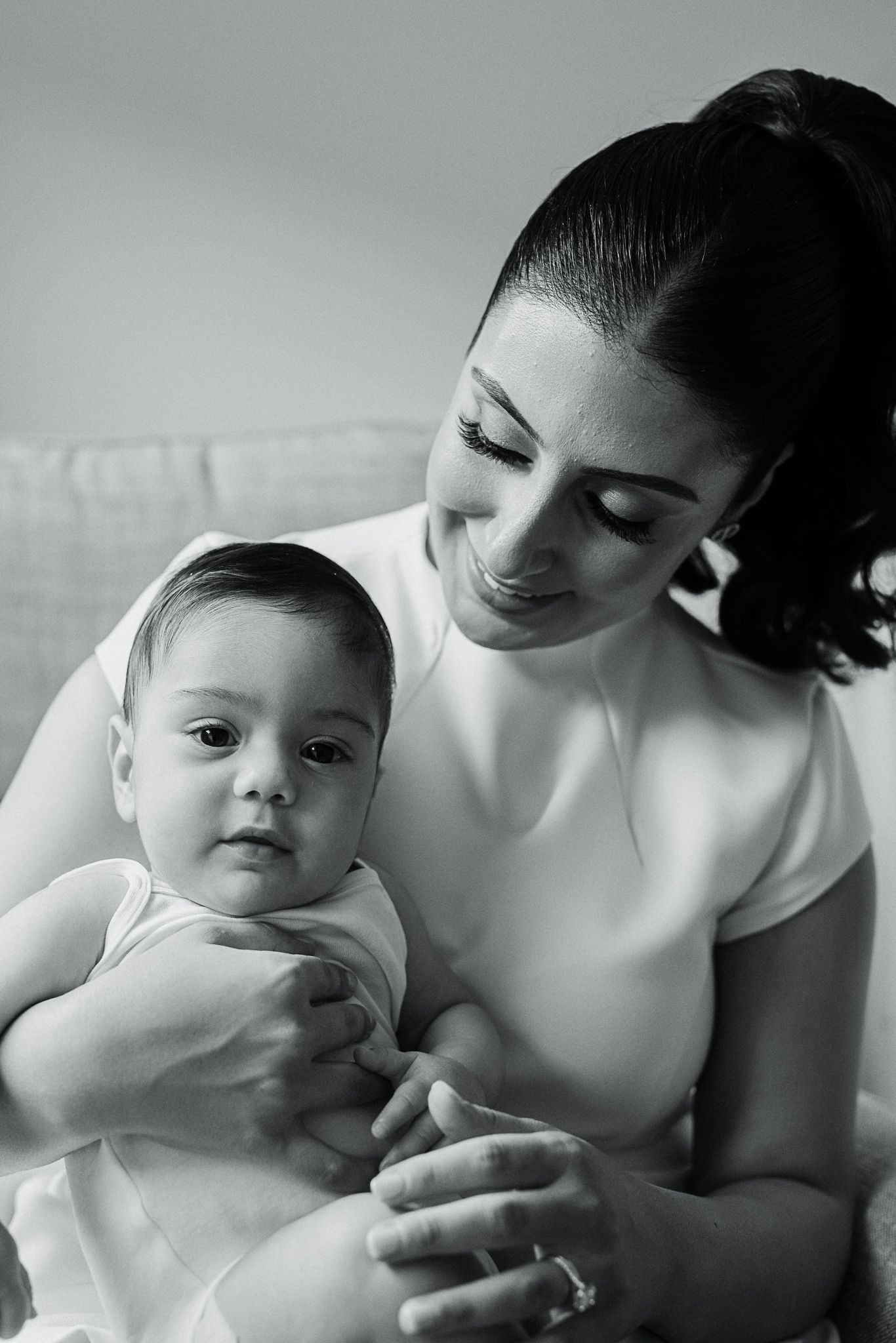 A black and white intimate portrait of a tender moment between a parent and baby in white clothing.