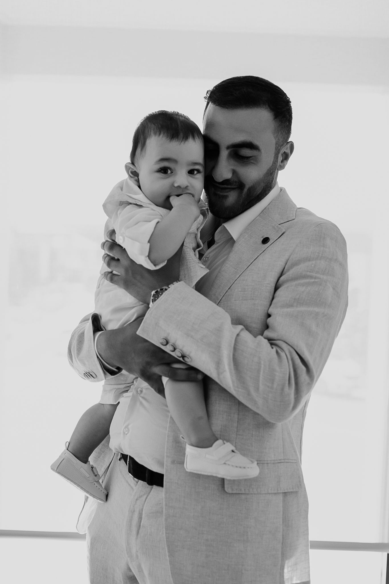 Black and white candid photo of man in suit holding and smiling at baby.