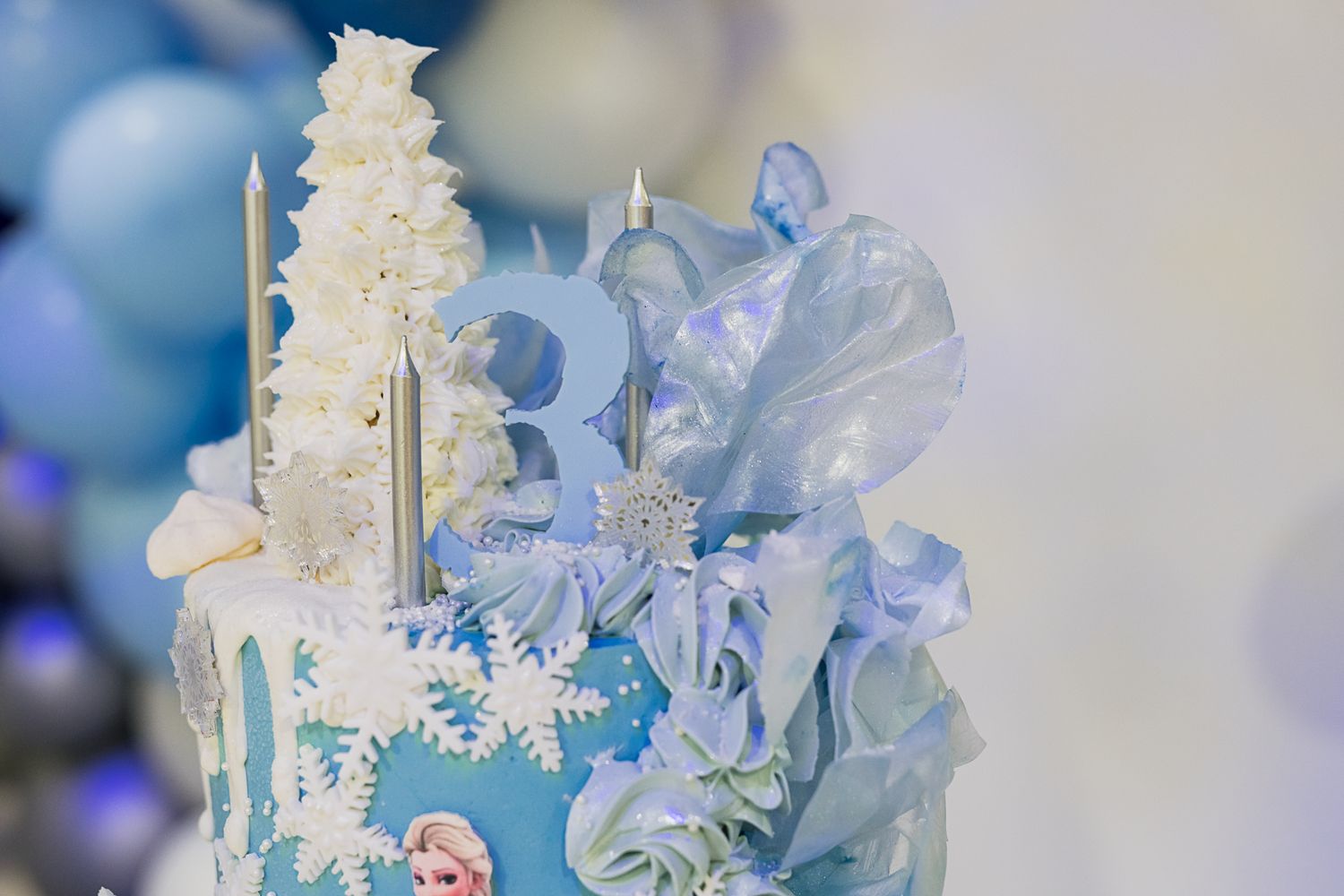 Elegant winter-themed cake with white snowflakes and blue ruffled frosting decorations.