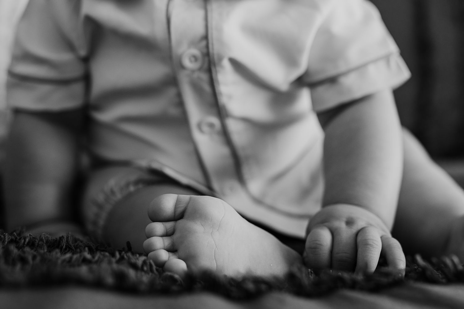 Black and white close-up of small hands resting on a textured carpet or blanket showing a child's tenderness.