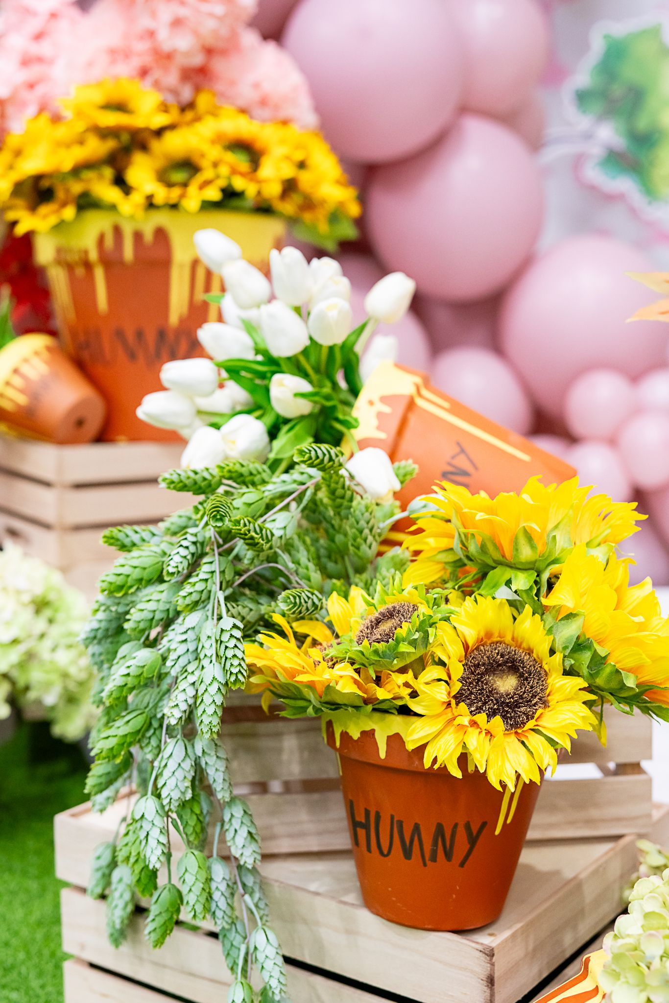 Rustic flower arrangement featuring sunflowers and greenery in terra cotta pots labeled 'HUNNY'.