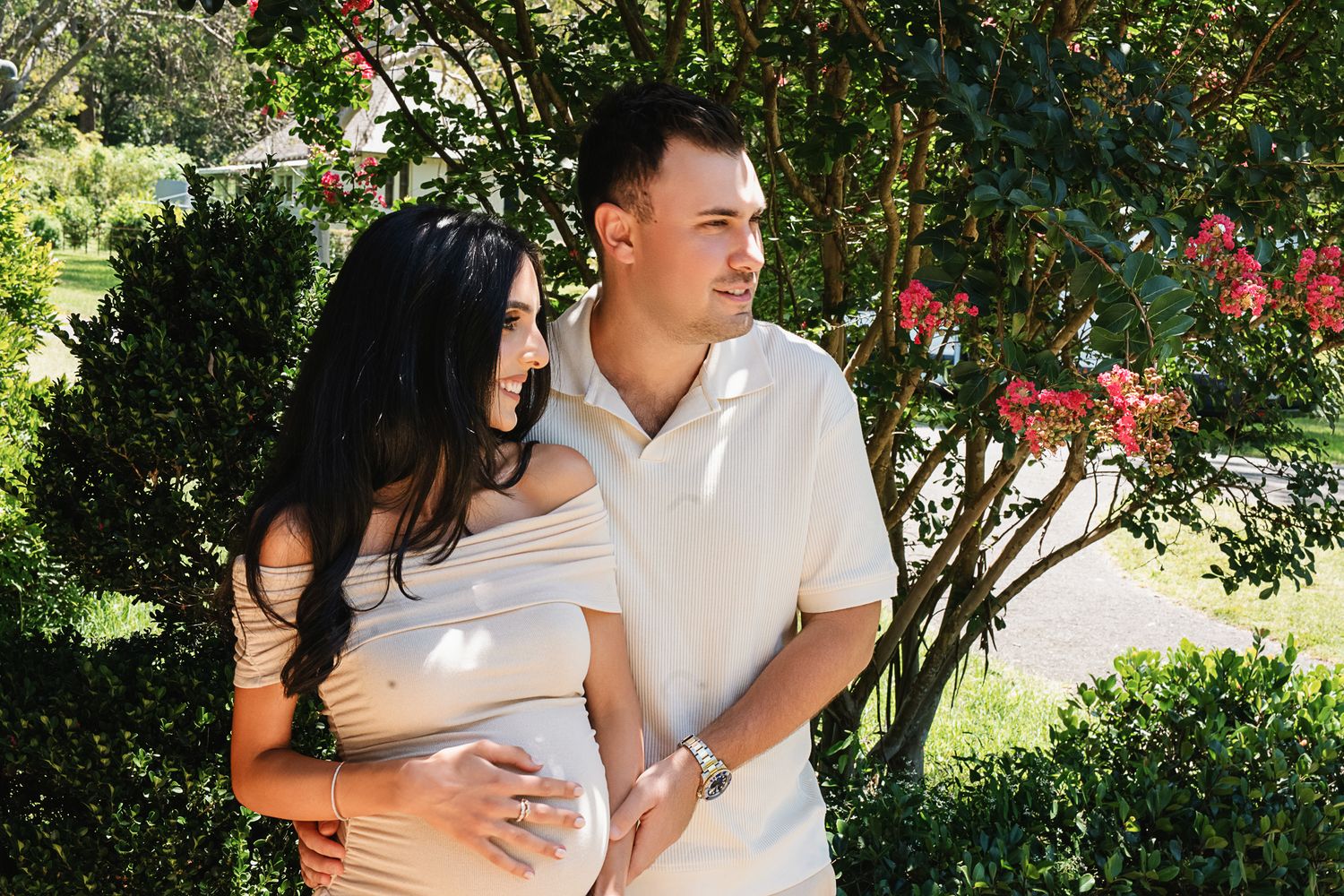 A tender moment between expecting parents as they smile in a garden setting.