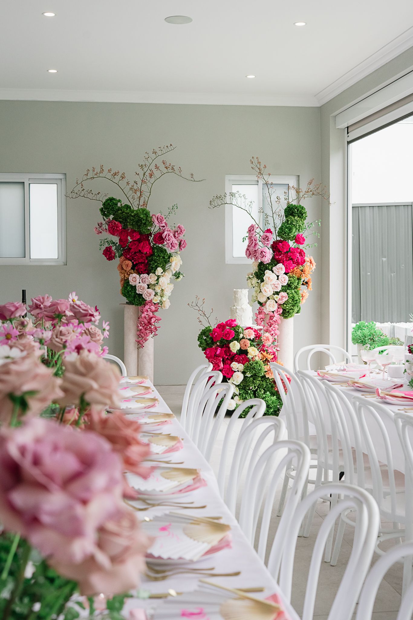 Indoor reception space with white chairs and stunning pink floral arrangements along dining tables.