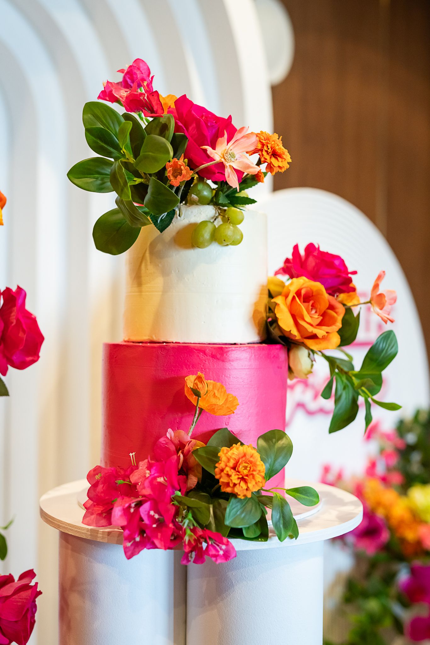 Colorful floral arrangement with pink and orange roses on tiered white and pink display pedestals.