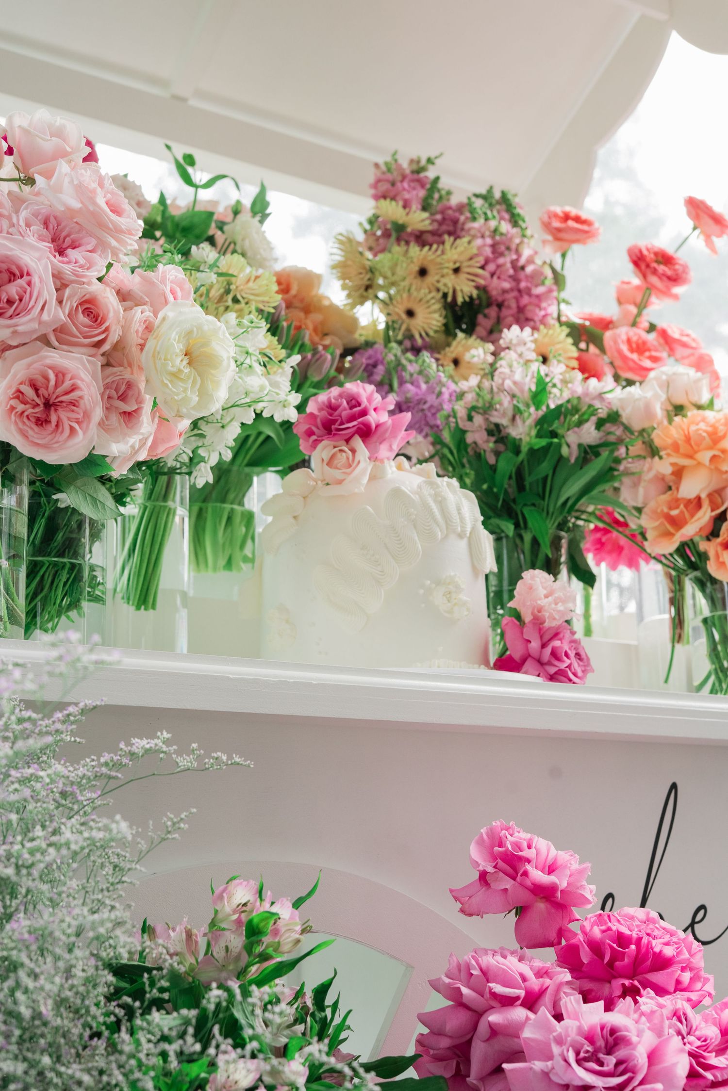 Luxurious pink and coral floral arrangements with roses and mixed blooms displayed on white modern shelf.