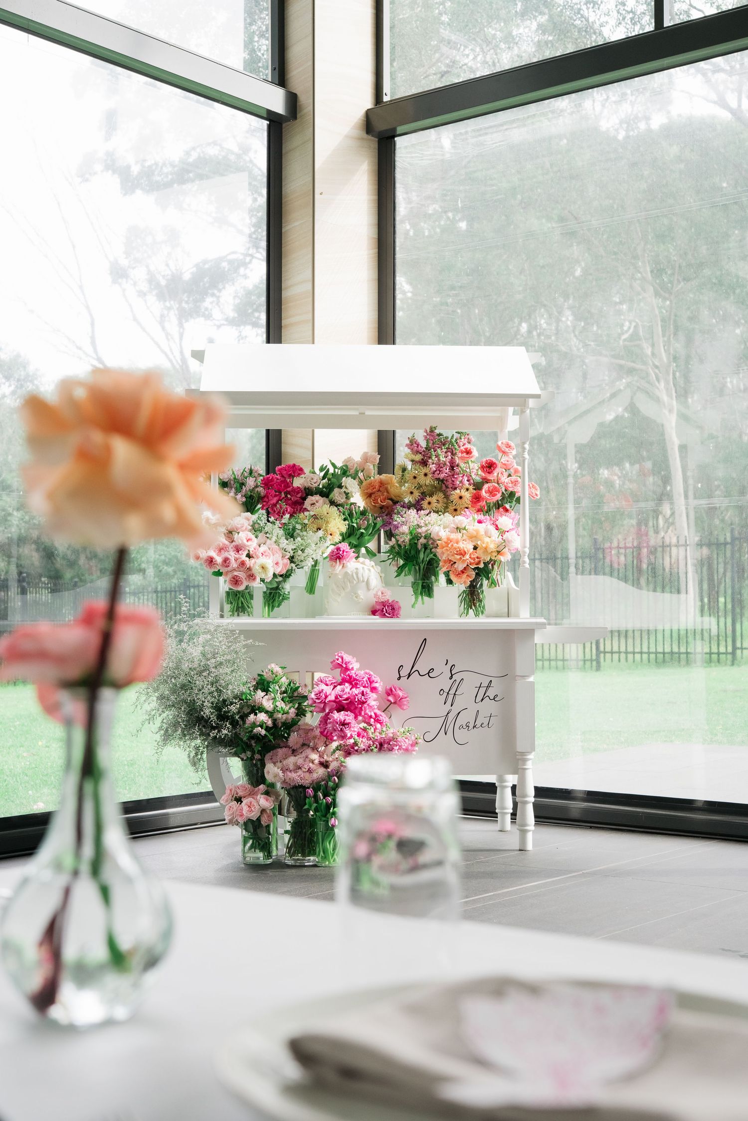 Elegant floral table setting with peach and pink flowers in glass vases along window ledge at wedding reception.