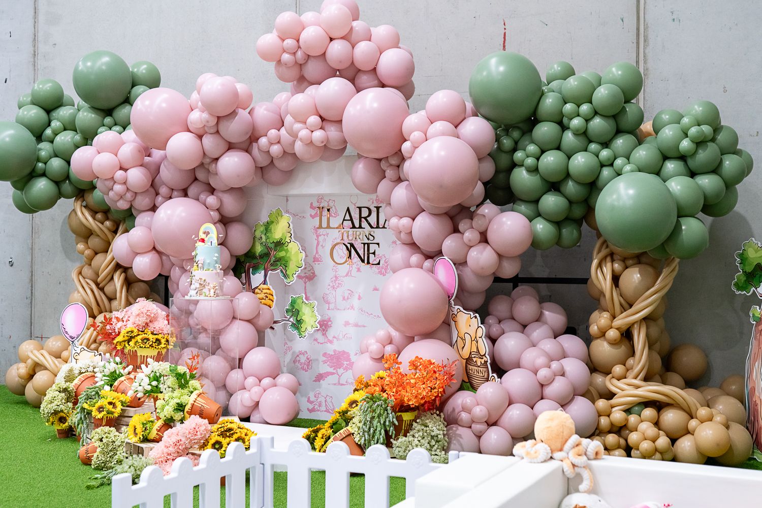 Enchanting party setup with balloon garland arch in pink and green, featuring floral arrangements and white fence.