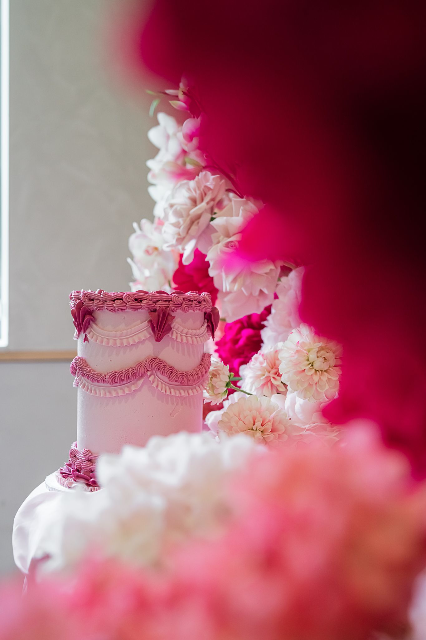 Elegant white wedding cake with pink piping details and floral decorations against a red background.