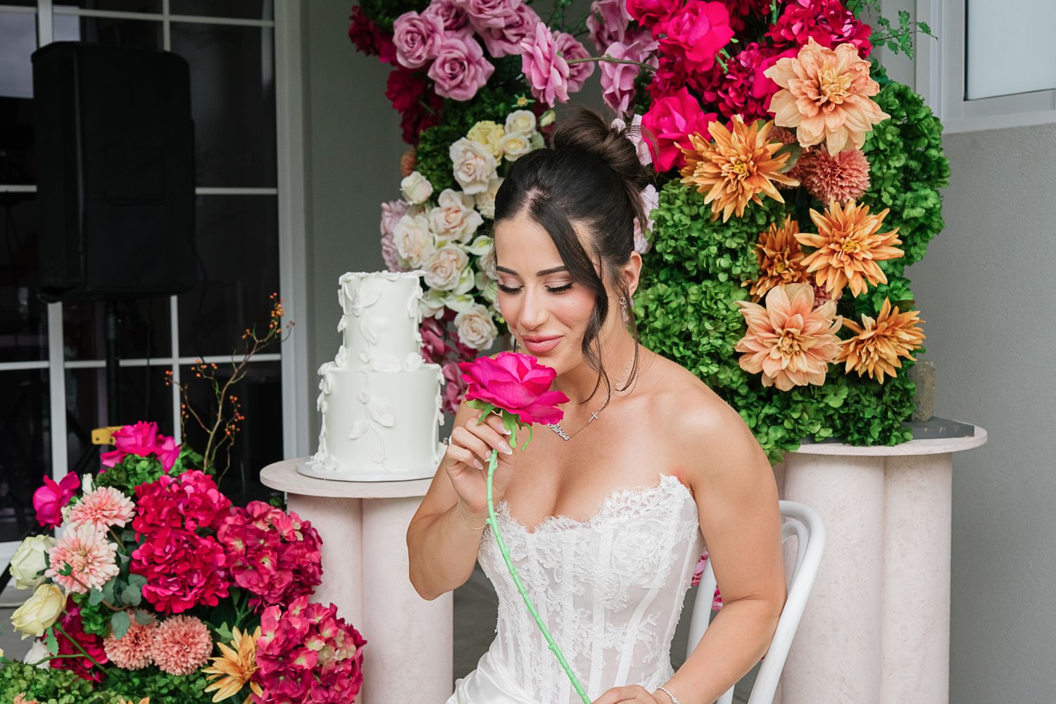 Elegant bridal portrait with white wedding cake and vibrant floral backdrop of pink and orange blooms.