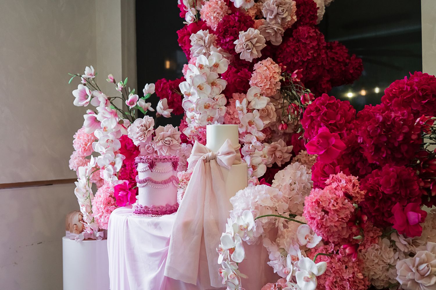 Luxurious wedding dessert table decorated with pink and red flowers and white fabric draping.