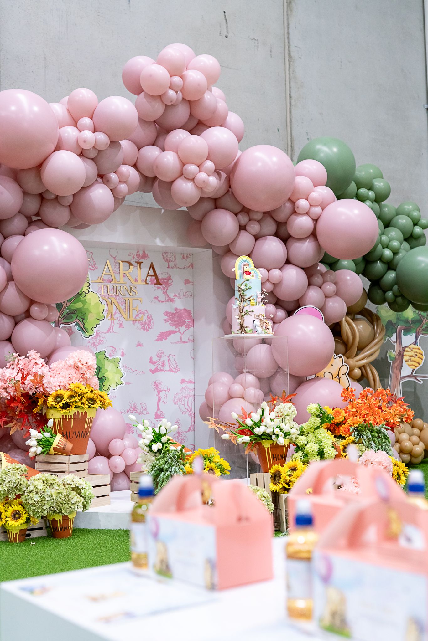 Pink and green balloon arch with vibrant flower arrangements and party favor boxes creating a whimsical backdrop.