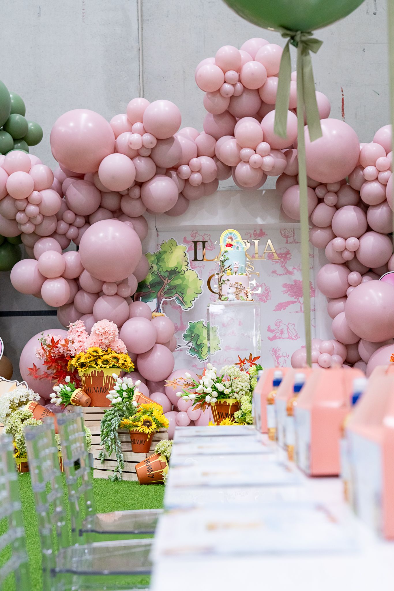 Elegant party setup with pink balloon arch, floral arrangements, and gift boxes along a decorated walkway.