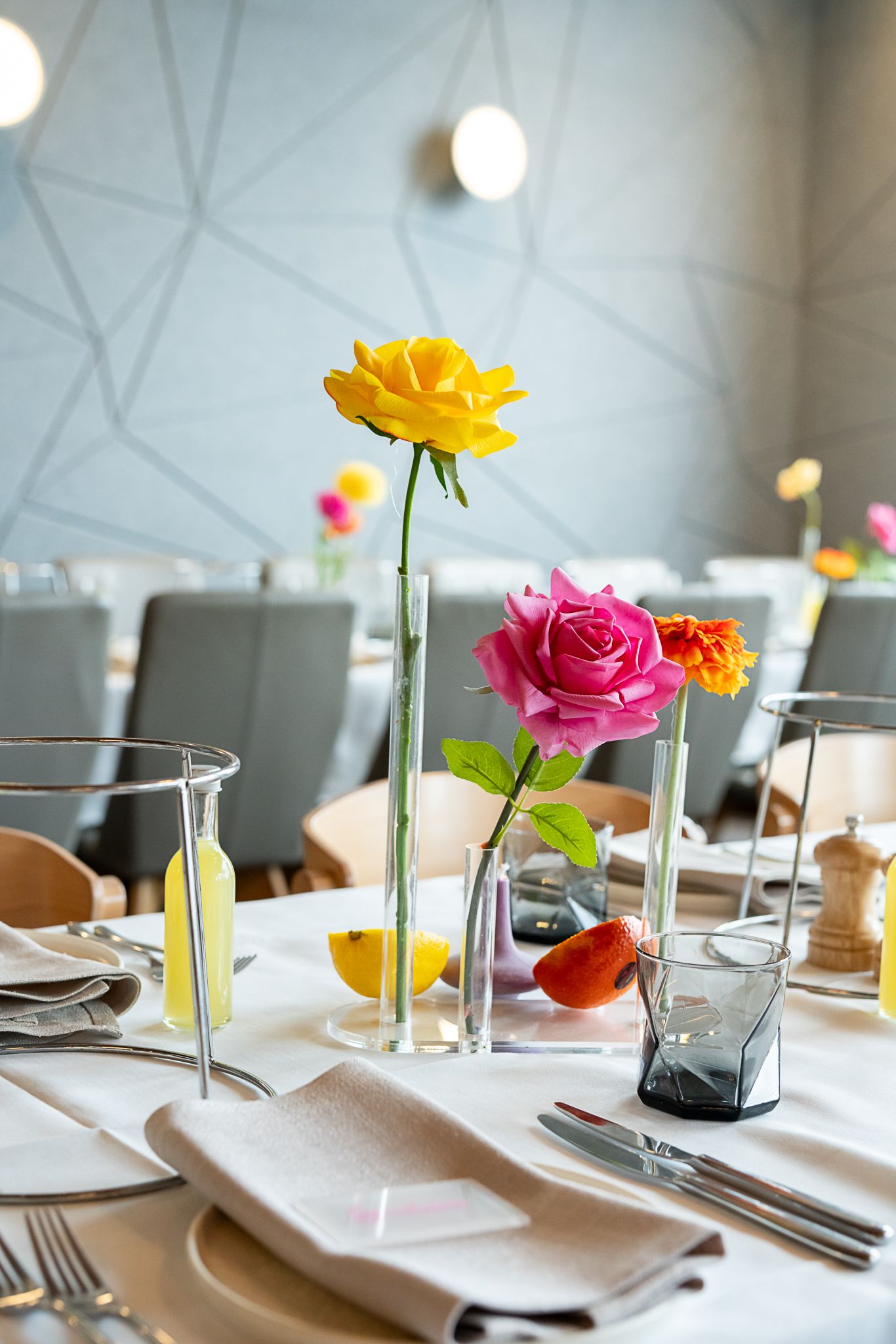 Modern table setting with yellow and pink roses in tall glass vases at a wedding reception.