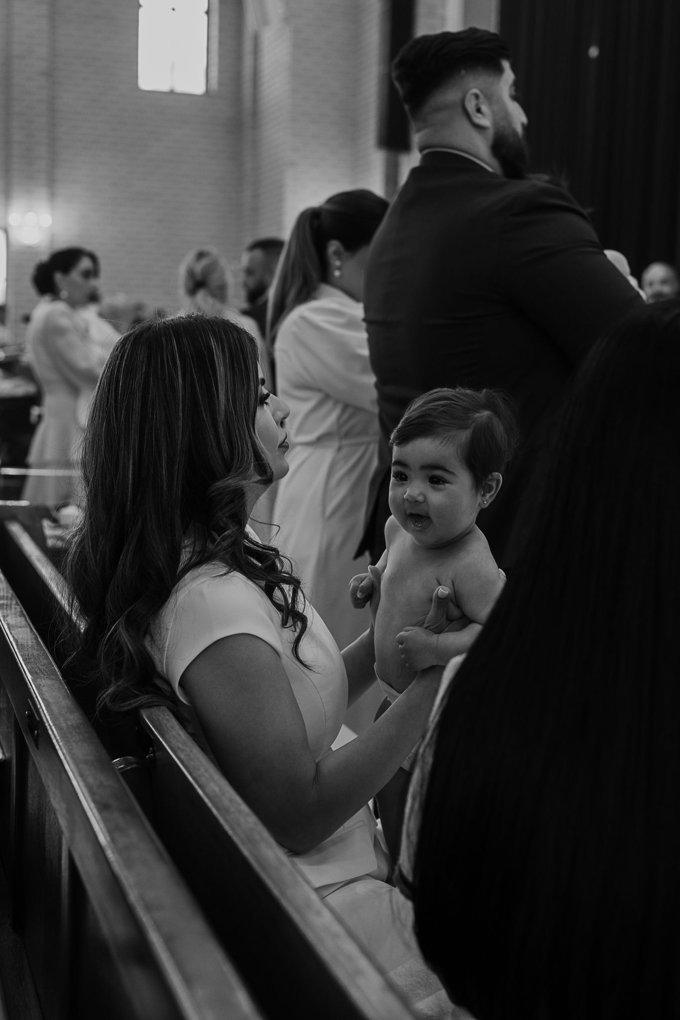 A candid black and white photo taken during a church ceremony showing attendees in the pews.