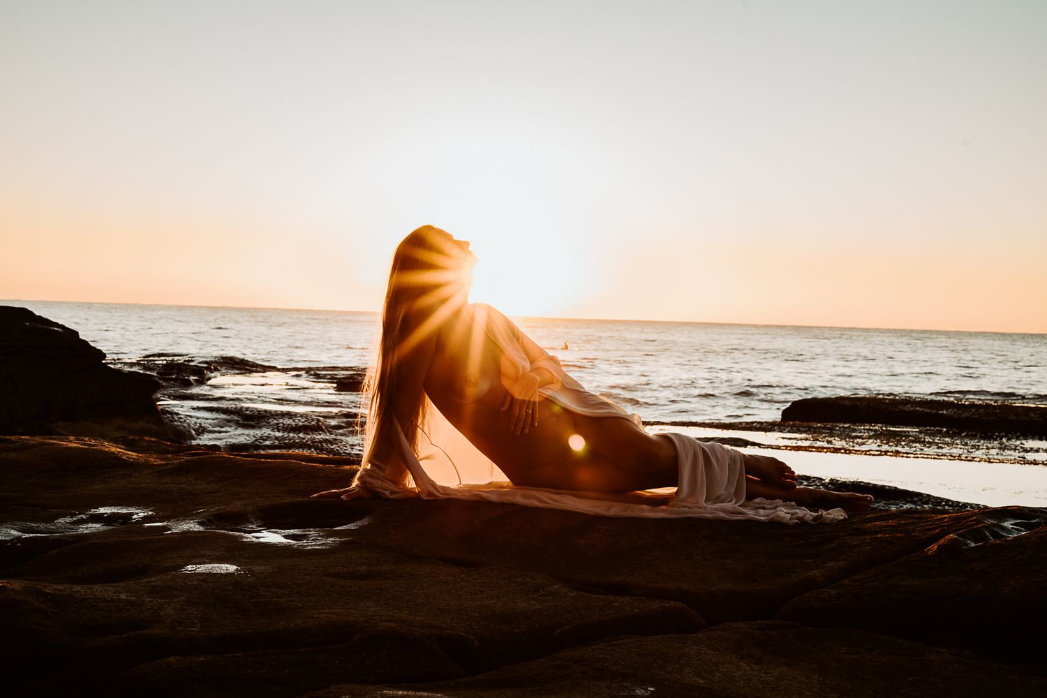 Silhouetted figure on beach rocks during golden sunset.