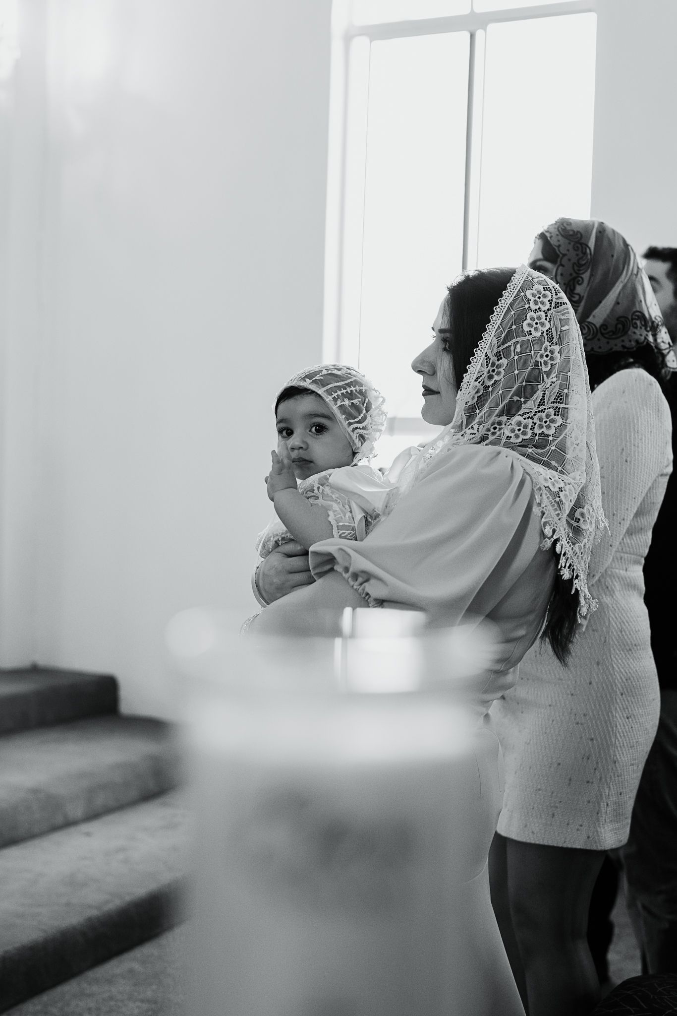 Baby in christening attire being held during religious ceremony.