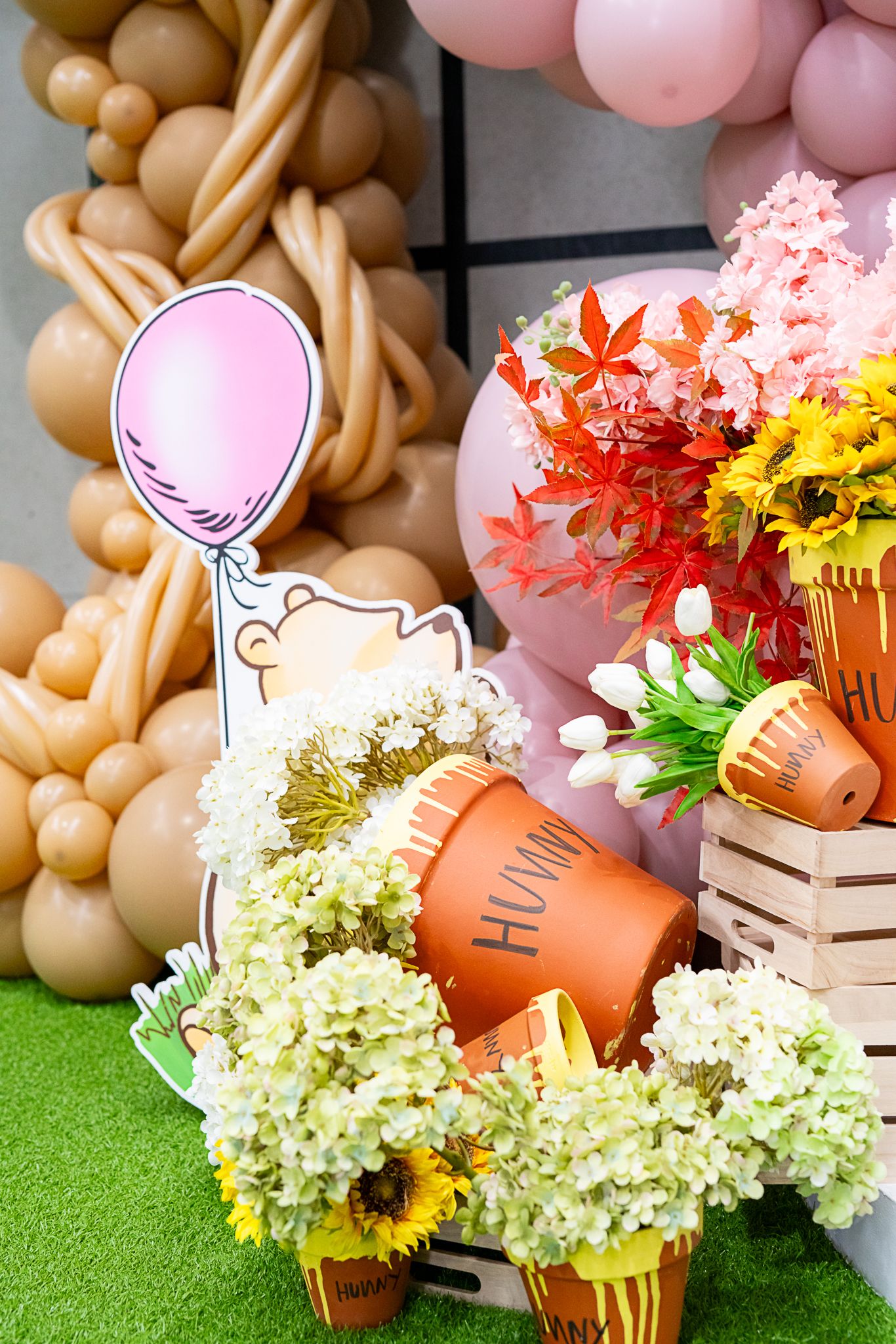 Winnie the Pooh themed decor with balloon art and floral arrangements on artificial grass.