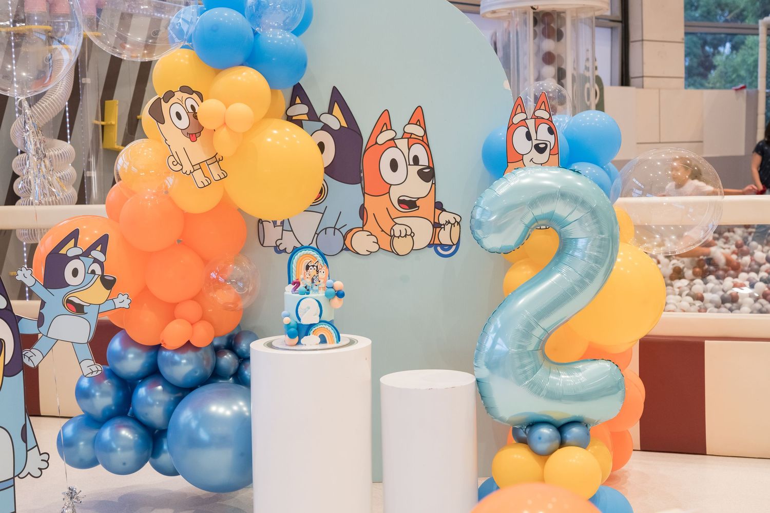 Children's party setup with Bluey characters, blue and orange balloons, and a large number 2 display.
