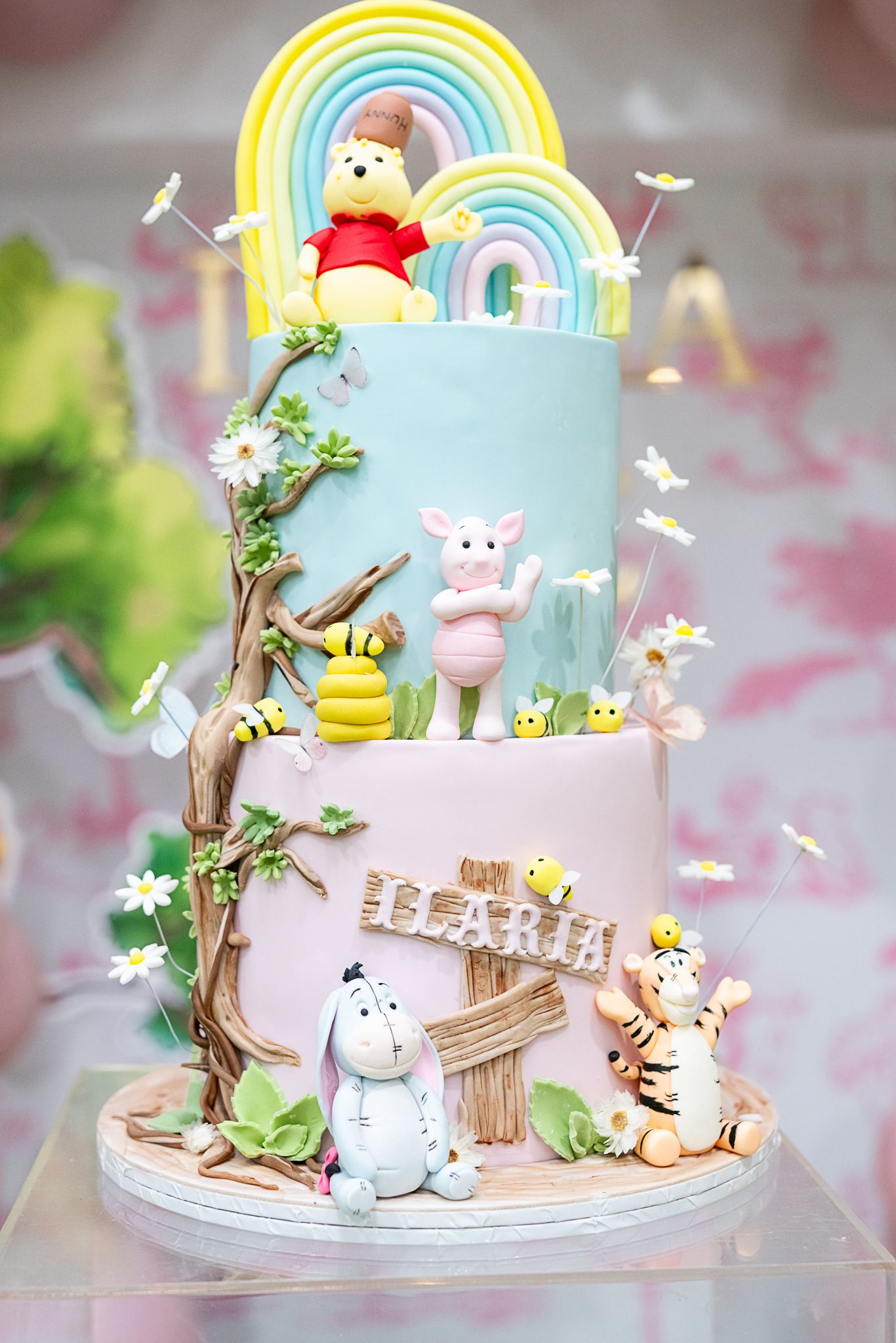 Two-tiered Winnie the Pooh themed cake with rainbow, honey bees, and woodland creatures.