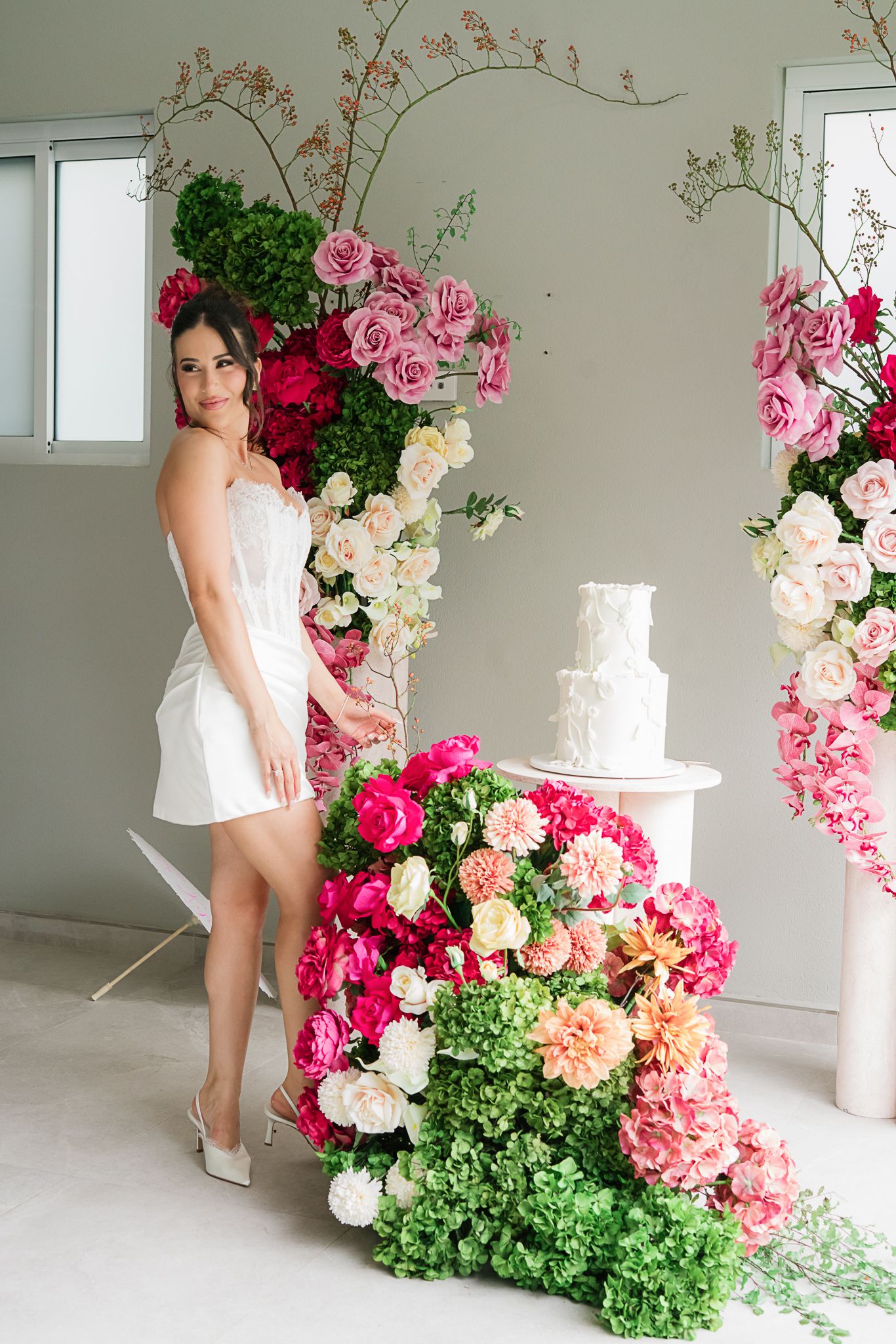 Elegant floral installation with pink and white roses surrounding a white wedding cake.