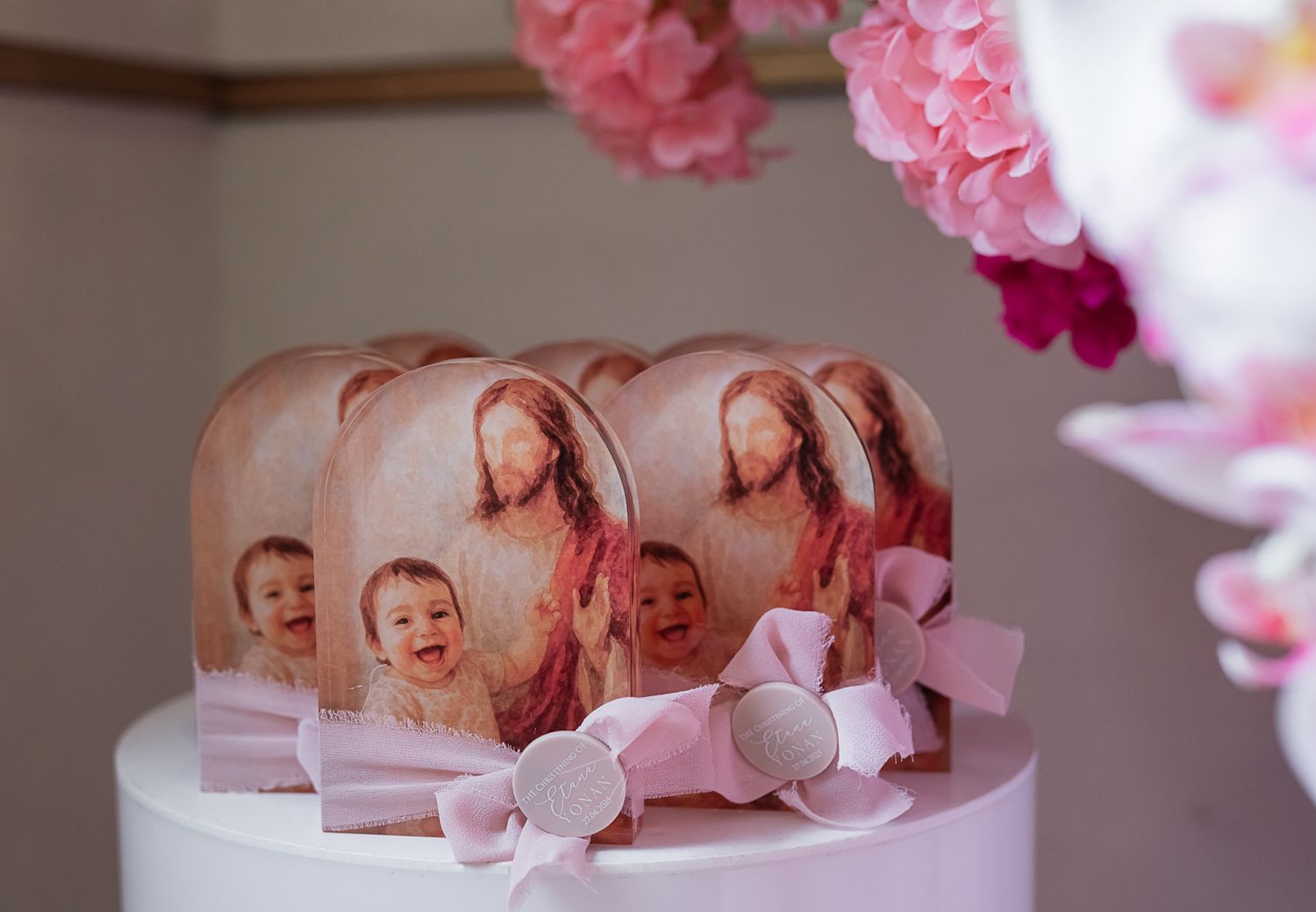 Decorated party favors featuring photo cutouts adorned with pink bows arranged on a white surface with floral decor above.