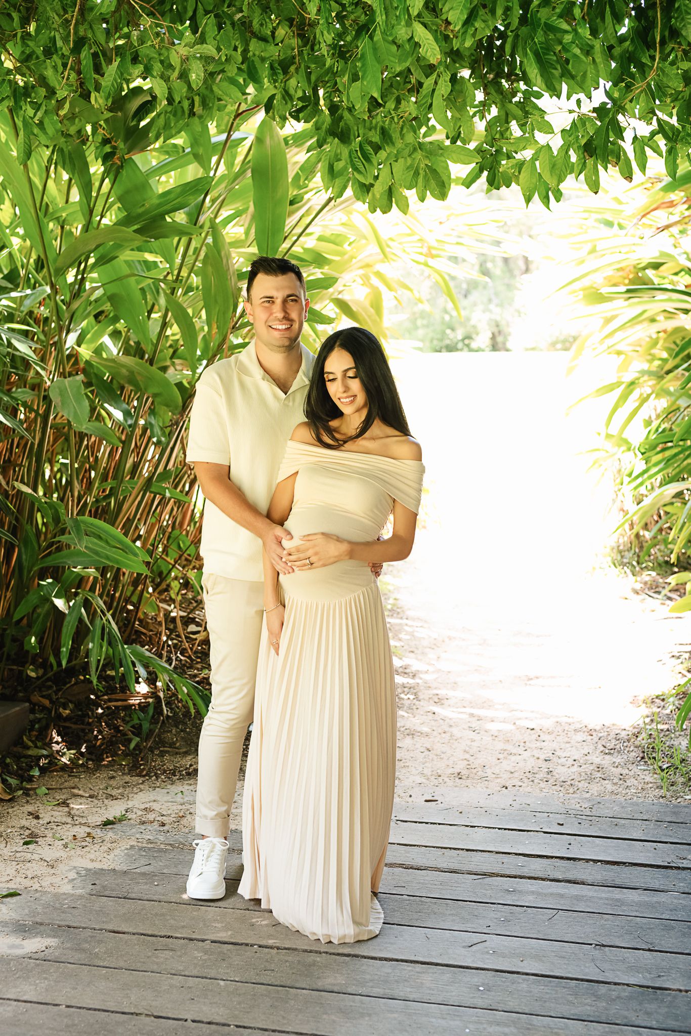 Couple in coordinating cream outfits pose together during outdoor maternity session.