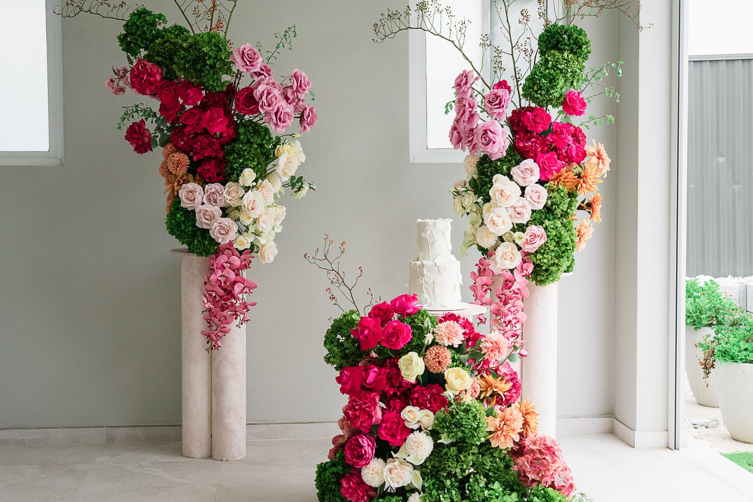 Three tall floral arrangements with pink, white and green flowers creating an elegant archway display.