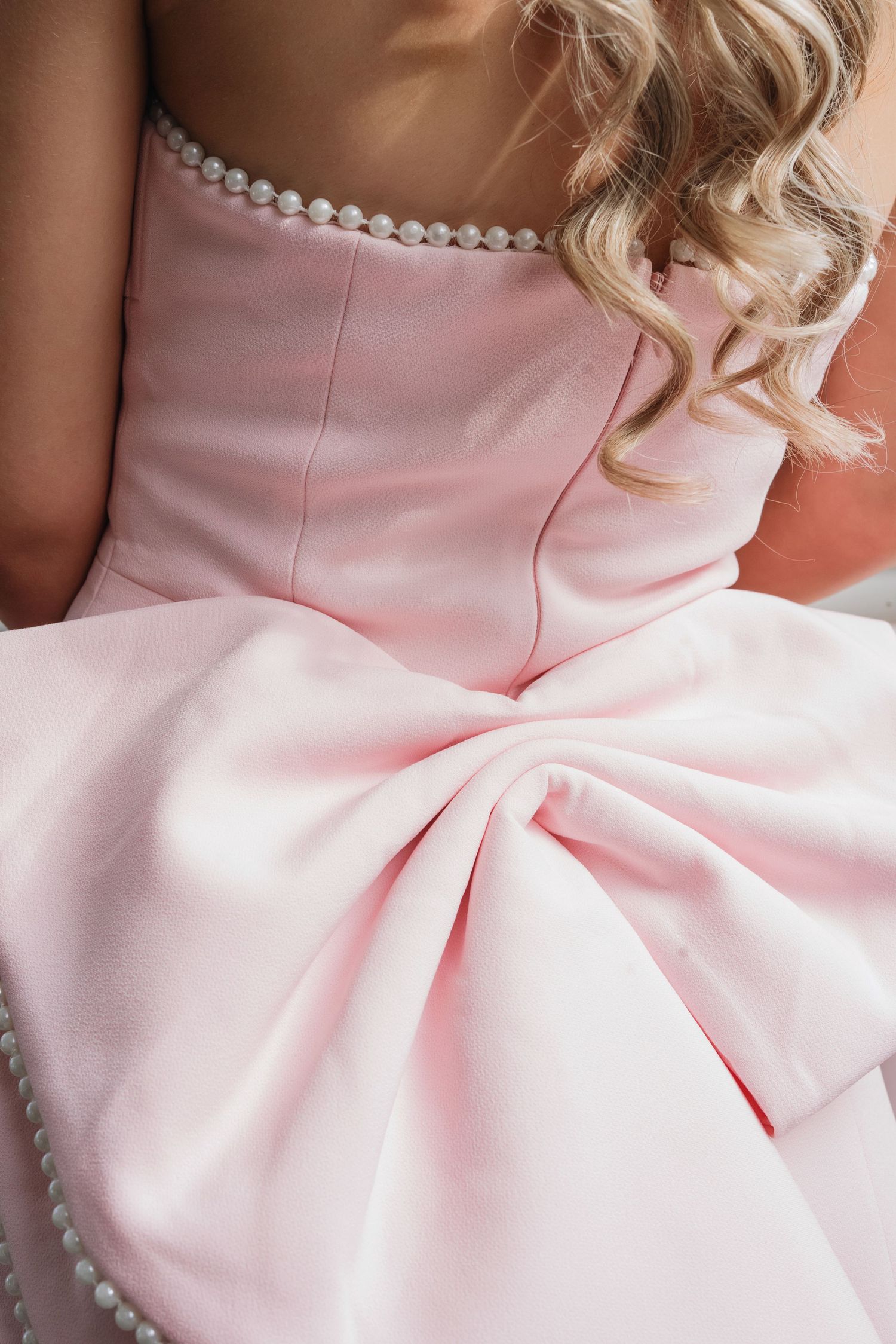 Elegant pale pink formal dress with pearl neckline detail and large decorative bow pleating at the waist.