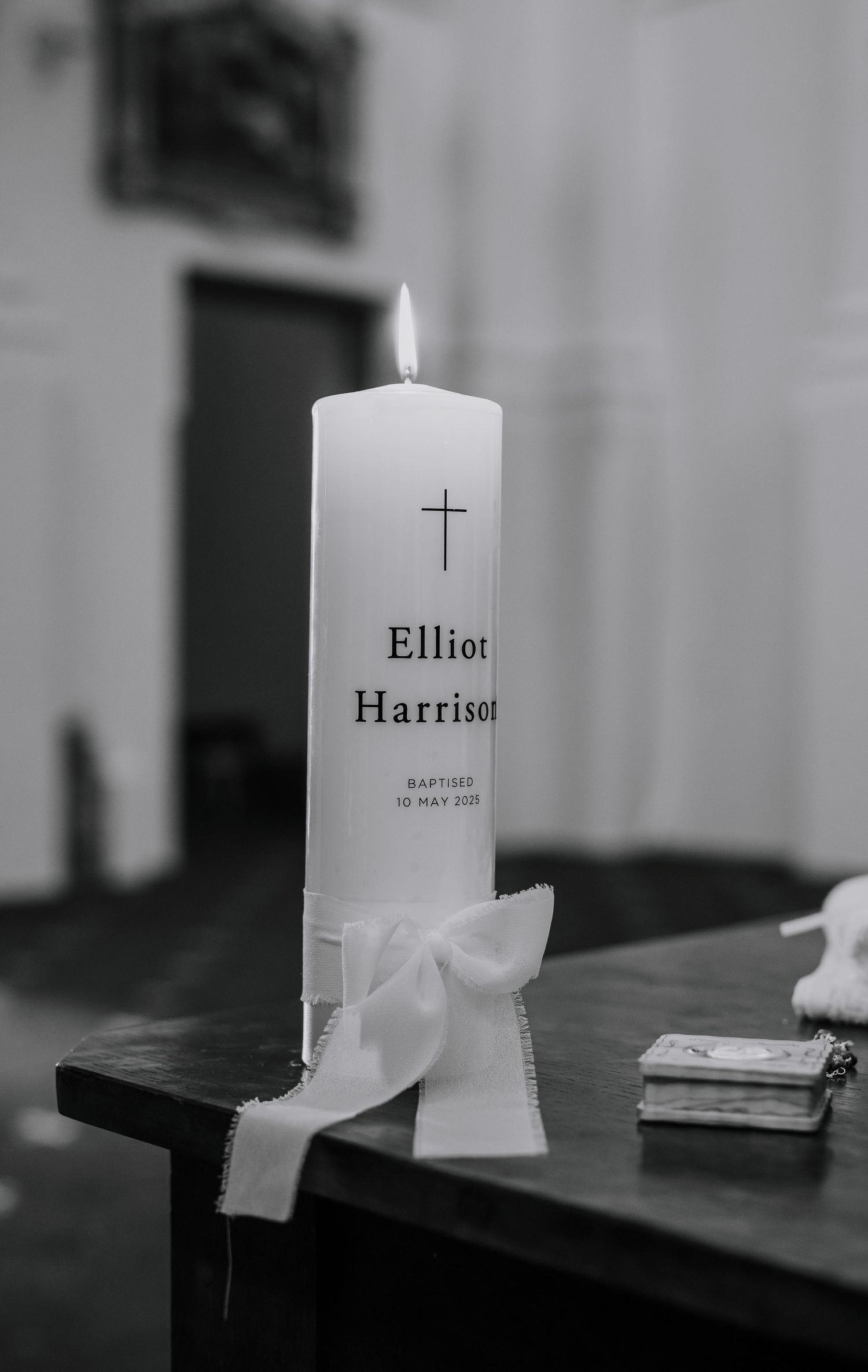 Lit baptismal candle with cross and name inscription against blurred background.