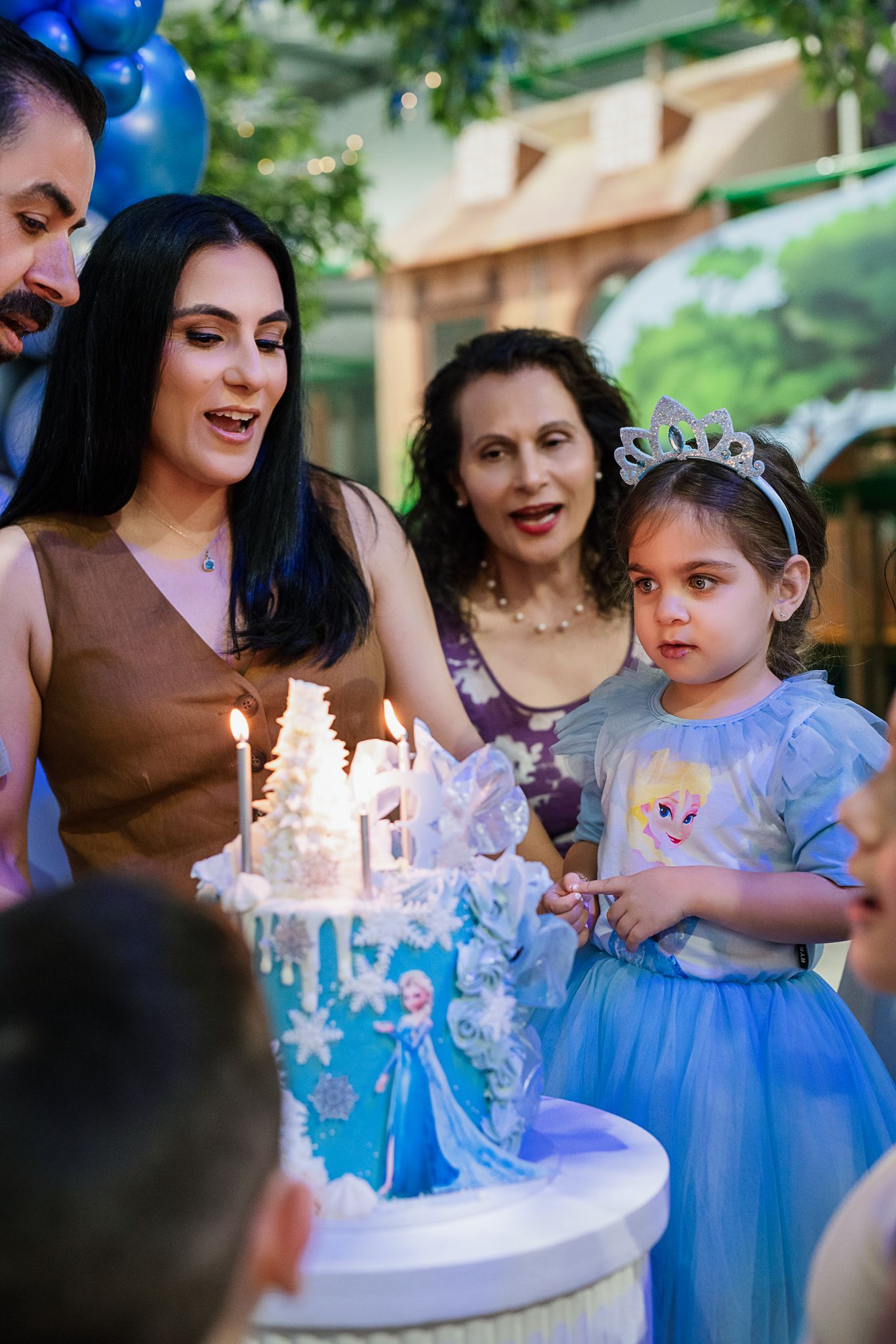 Family gathered around a blue and white Frozen-themed birthday cake at an outdoor celebration.